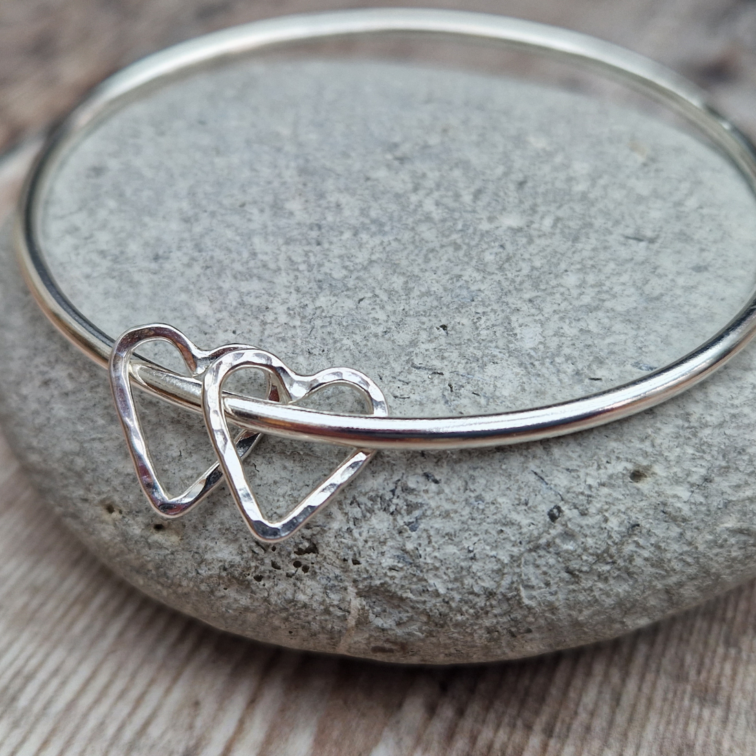 Silver Open Heart Bangle shown displayed on a grey stone.