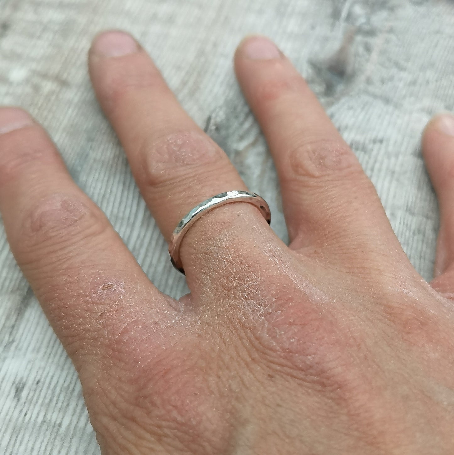 A sterling silver hammered ring worn on a finger, showcasing its simple yet elegant design with a subtle textured finish.