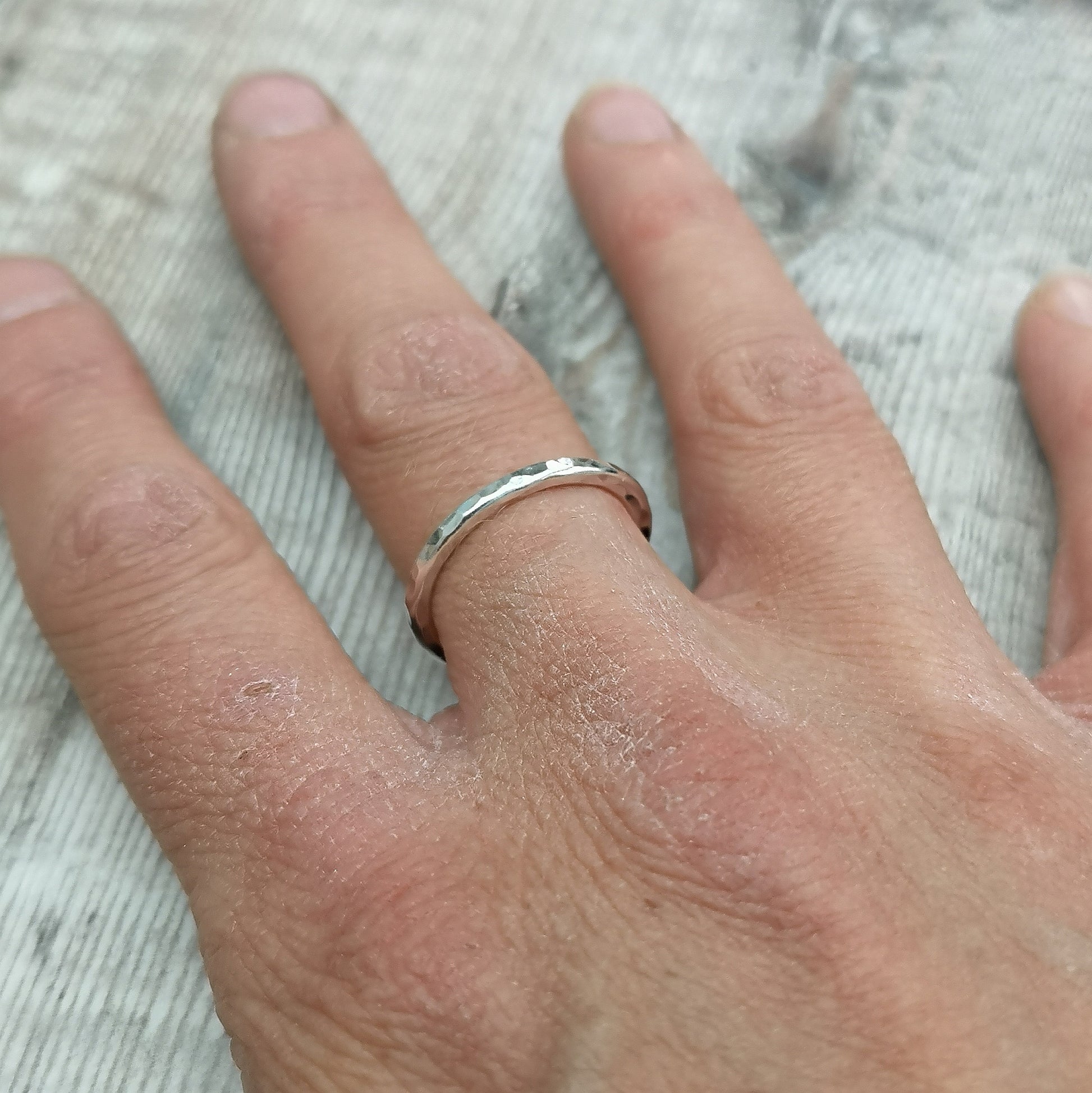 A sterling silver hammered ring worn on a finger, showcasing its simple yet elegant design with a subtle textured finish.