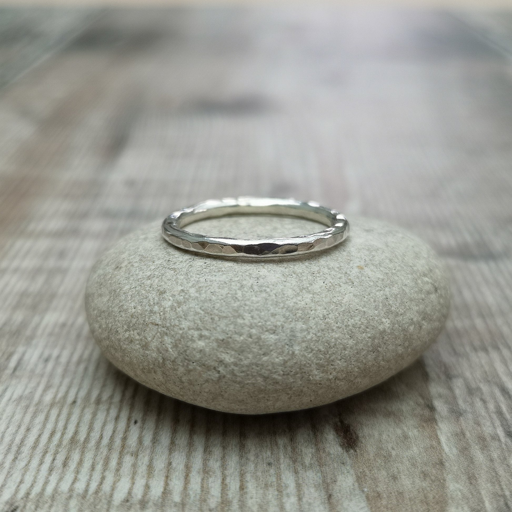 A close-up of a sterling silver hammered ring resting on a smooth stone, highlighting the ring’s delicate 2mm band and textured surface.
