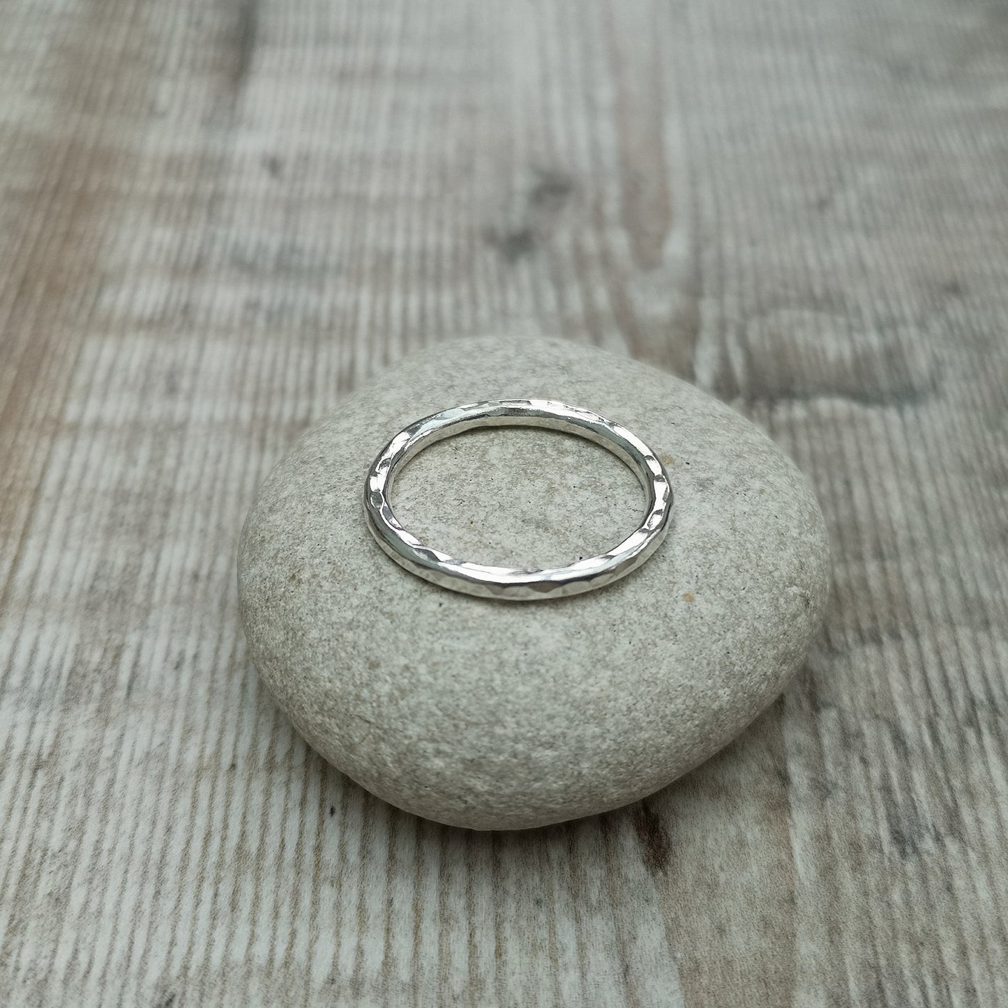 A close-up of a sterling silver hammered ring resting on a smooth stone, highlighting the ring’s delicate 2mm band and textured surface.