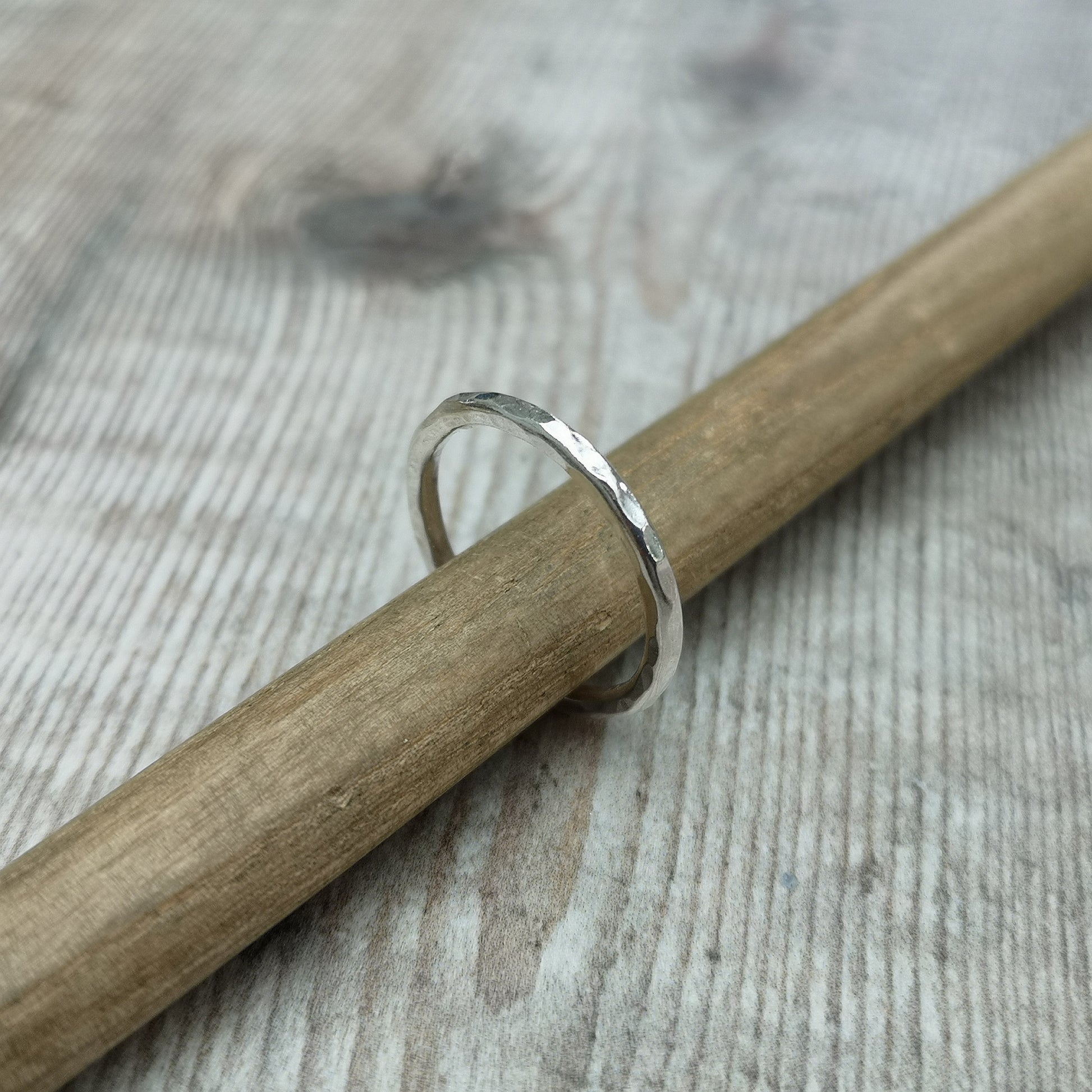 A sterling silver hammered ring balanced on a wooden stick, showcasing the handcrafted details of its 2mm band and its polished, textured surface.
