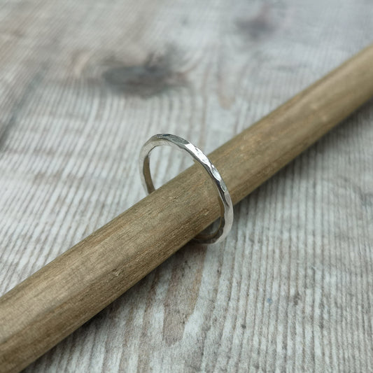 A sterling silver hammered ring balanced on a wooden stick, showcasing the handcrafted details of its 2mm band and its polished, textured surface.
