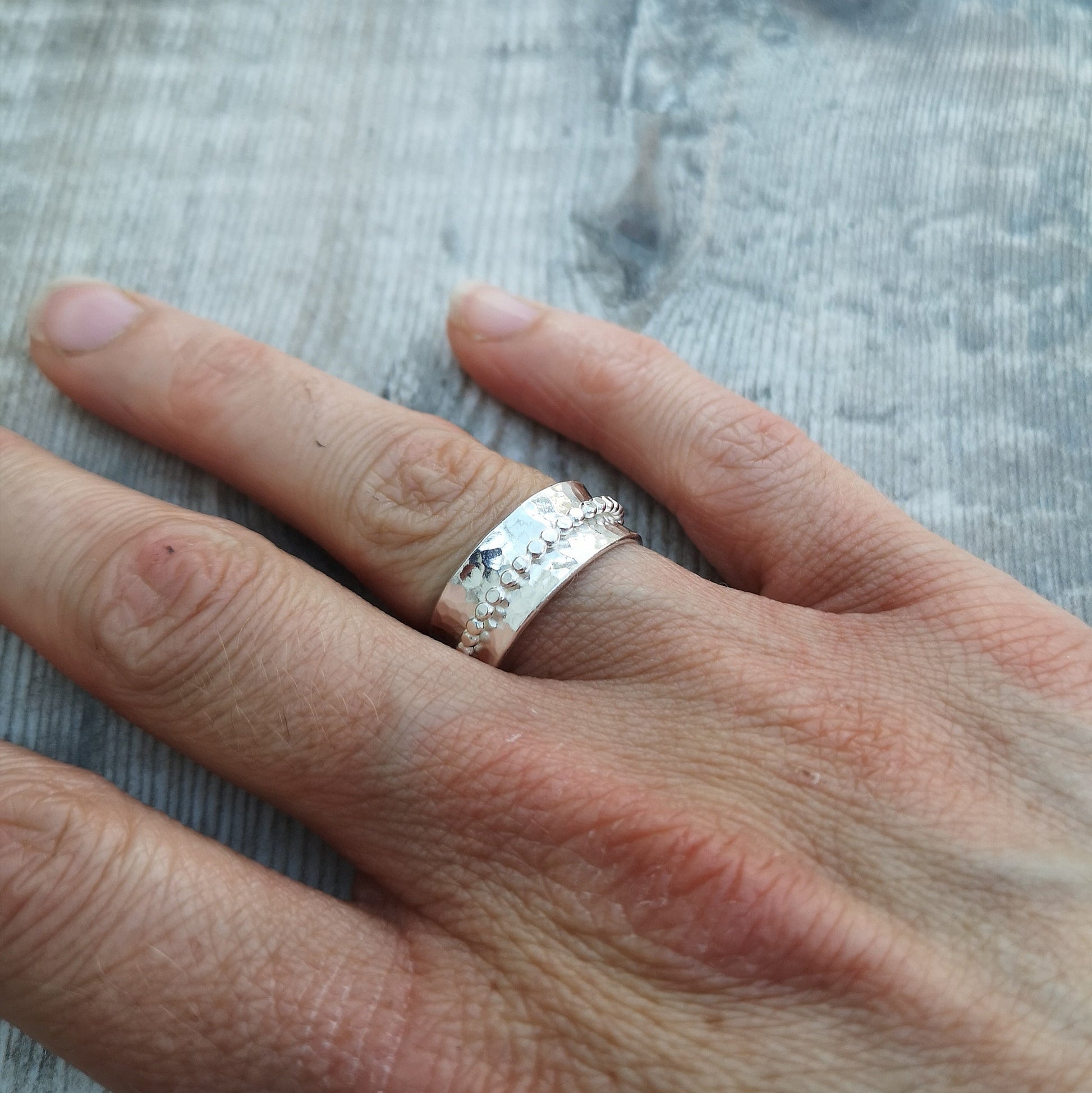 Approx. 8mm wide hammered texture silver band with additional 2mm wide silver beaded band around the middle that spins independently.