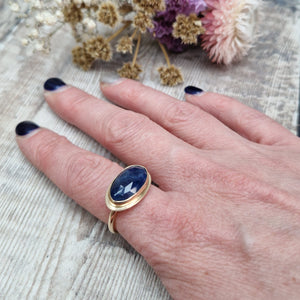 9ct gold ring with dark blue colour sapphire gemstone, oval shaped. Set in raised gold surround. Gemstone set lengthways across ring. Slight texture to stone, like diamond cut.