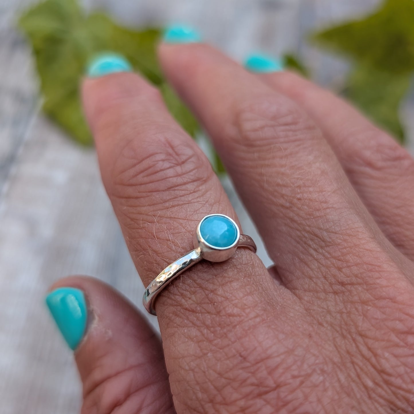 amazonite ring size R worn on a finger, highlighting the hammered recycled Sterling Silver band and the bright blue green Amazonite gemstone.
