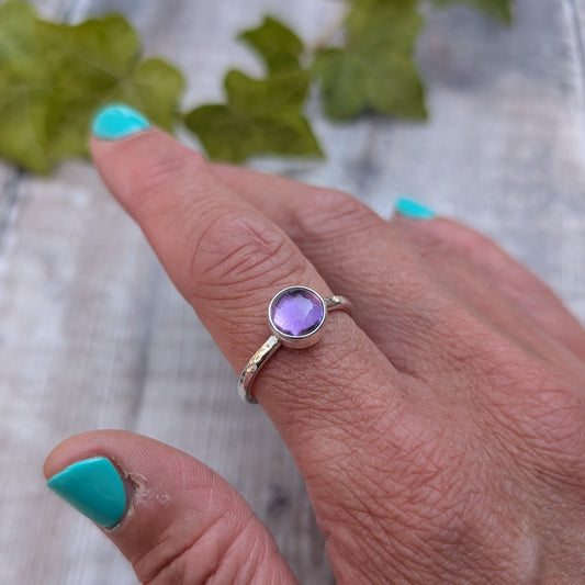 Amethyst ring size S handmade from recycled Sterling Silver, worn on a finger showing the round purple Amethyst gemstone in a simple bezel setting.