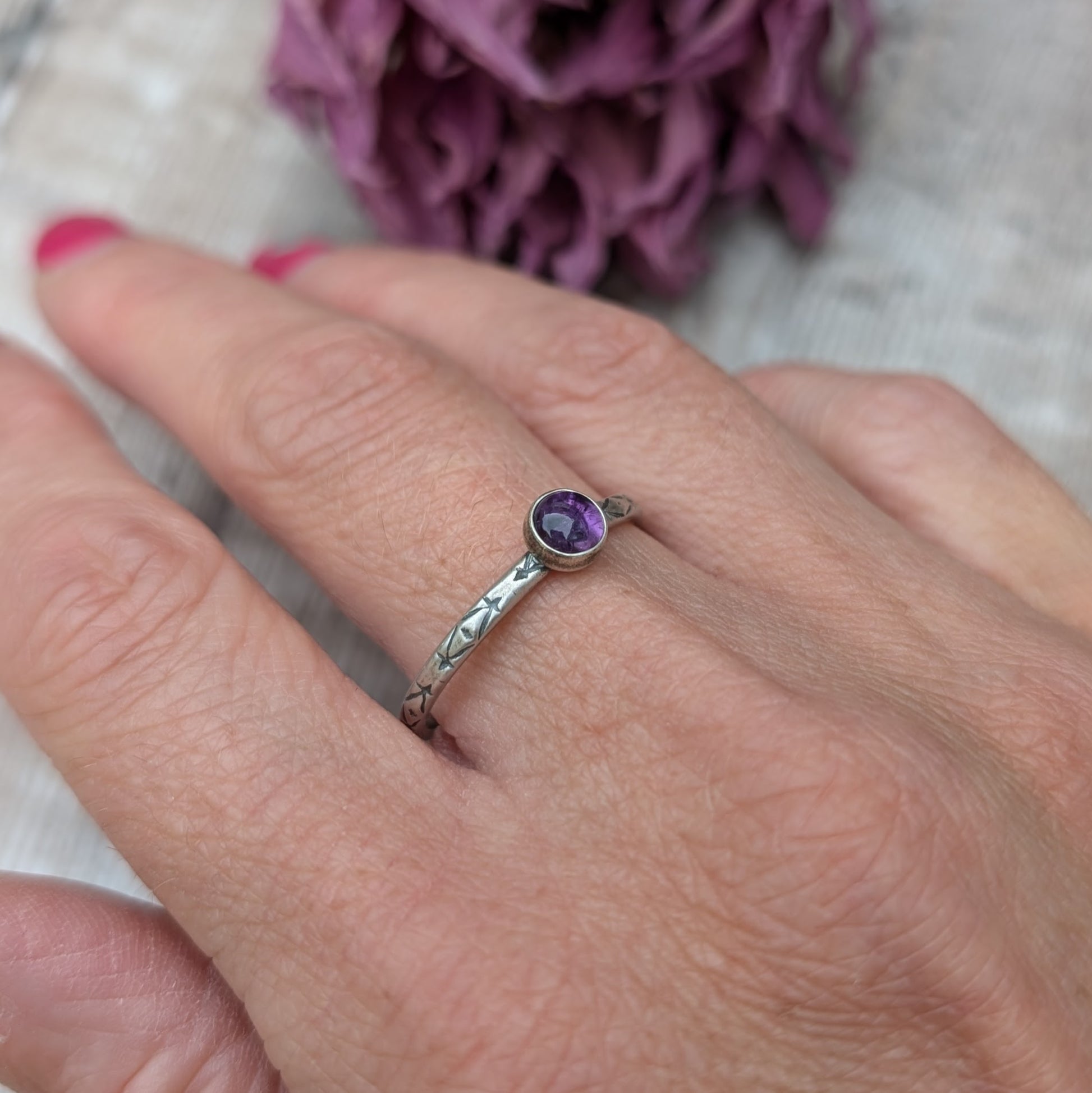 Slim silver band with cross stamped pattern. A purple Amethyst round stone is mounted on the band in an oxidised sterling silver bezel. Rings can be stacked above or below this piece.