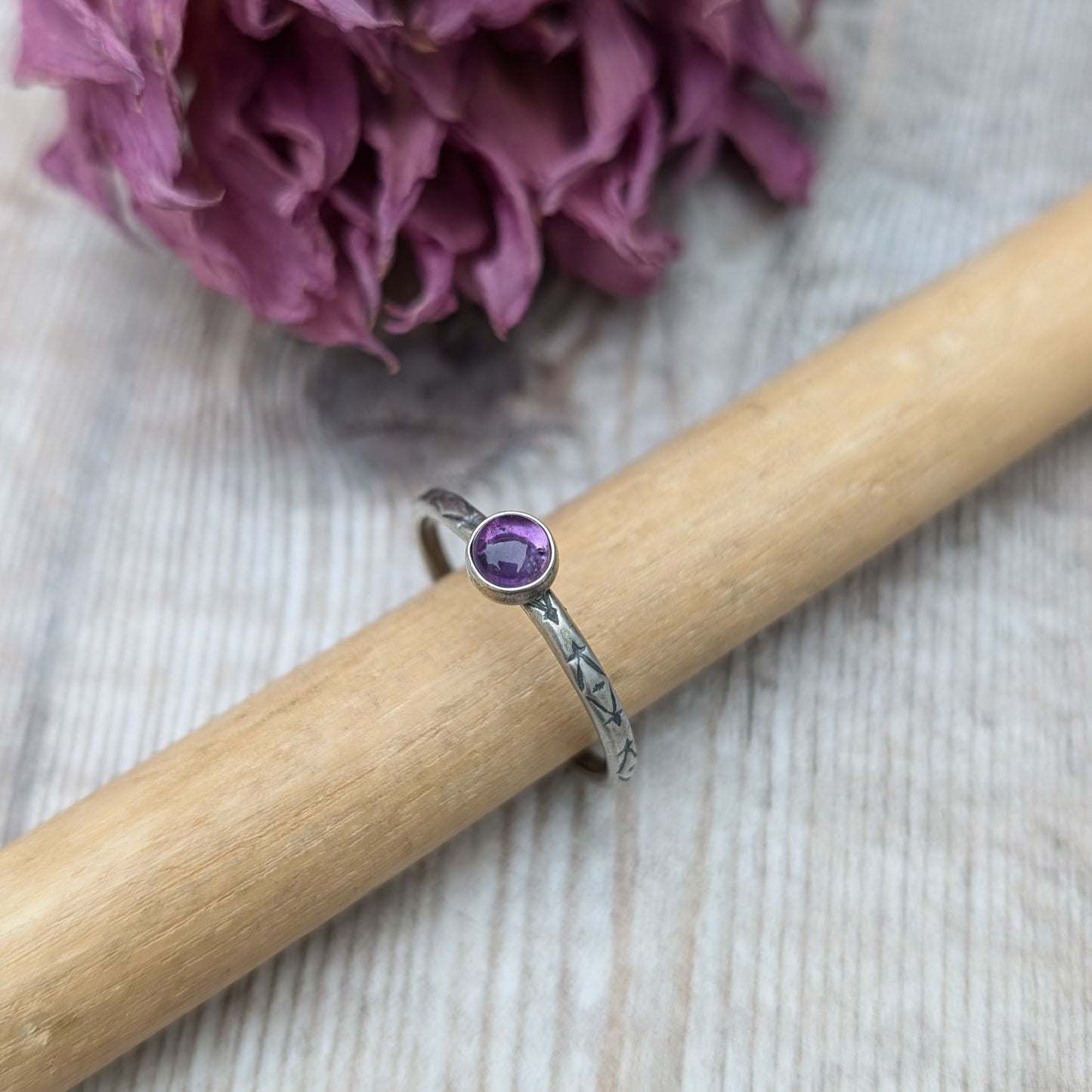 Slim silver band with cross stamped pattern. A purple Amethyst round stone is mounted on the band in an oxidised sterling silver bezel. Rings can be stacked above or below this piece.