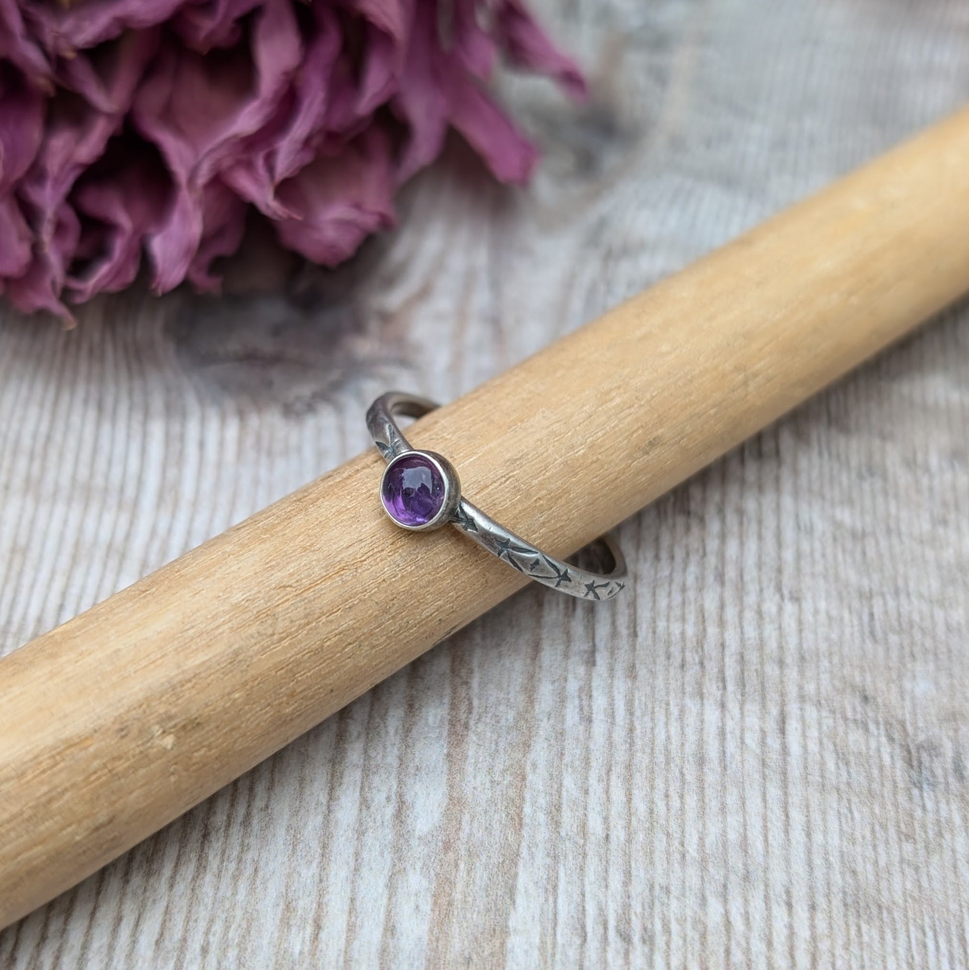 Slim silver band with cross stamped pattern. A purple Amethyst round stone is mounted on the band in an oxidised sterling silver bezel. Rings can be stacked above or below this piece.