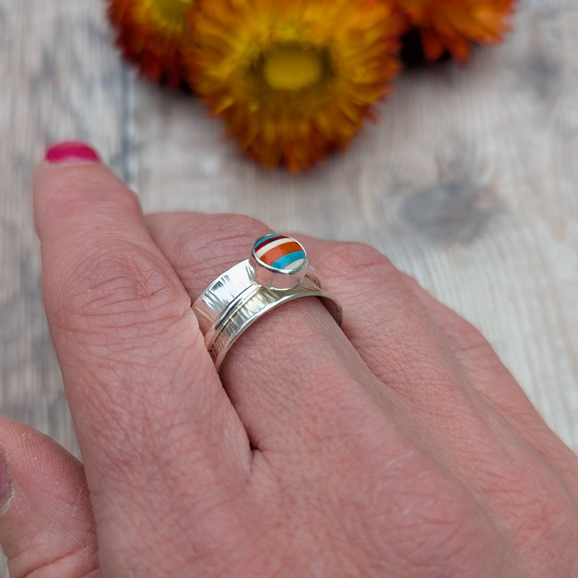Close-up of a hand wearing a bark textured sterling silver spinner ring set with a striped Surfite stone.