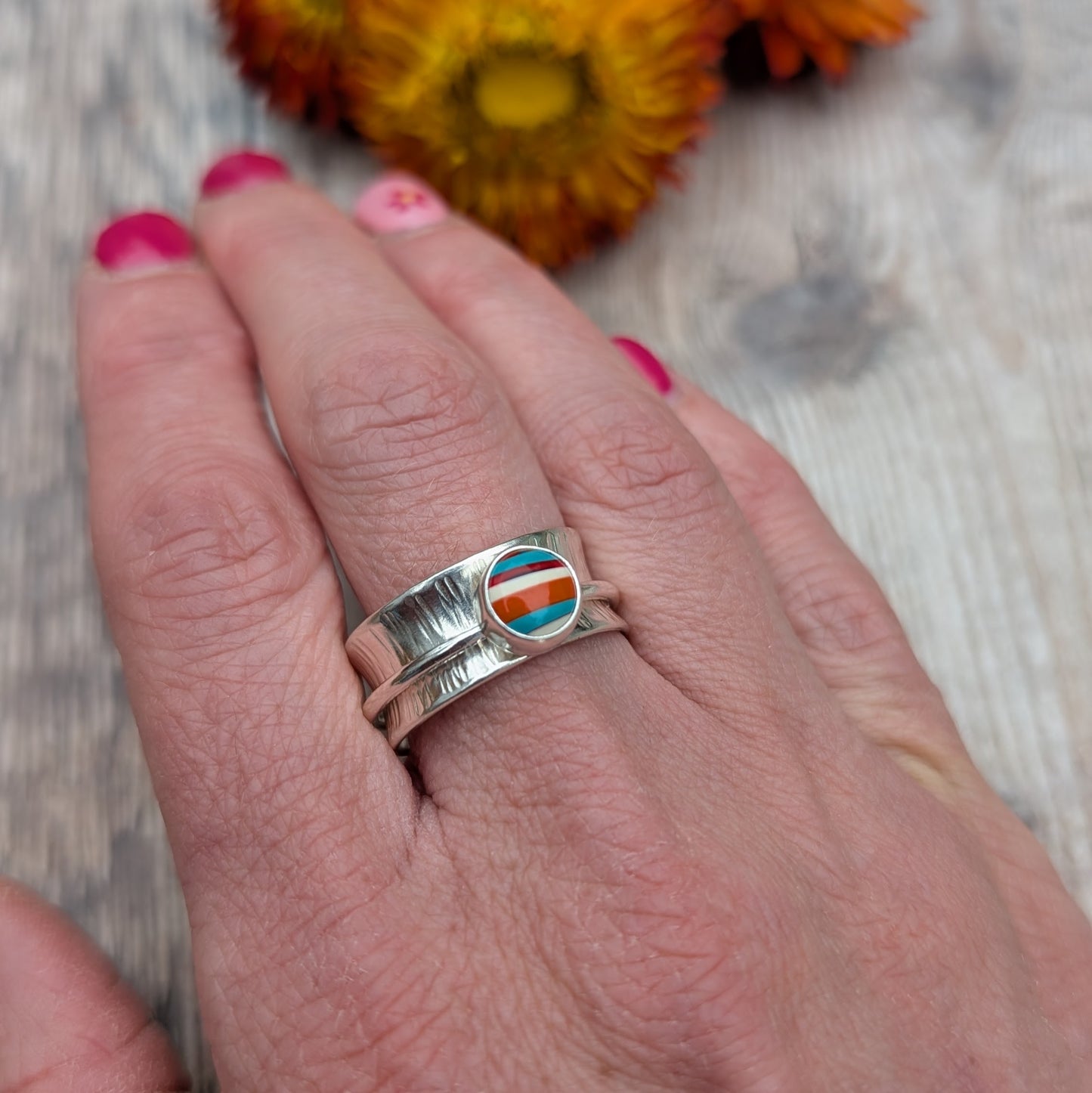 Close-up of a hand wearing a bark textured sterling silver spinner ring set with a striped Surfite stone.