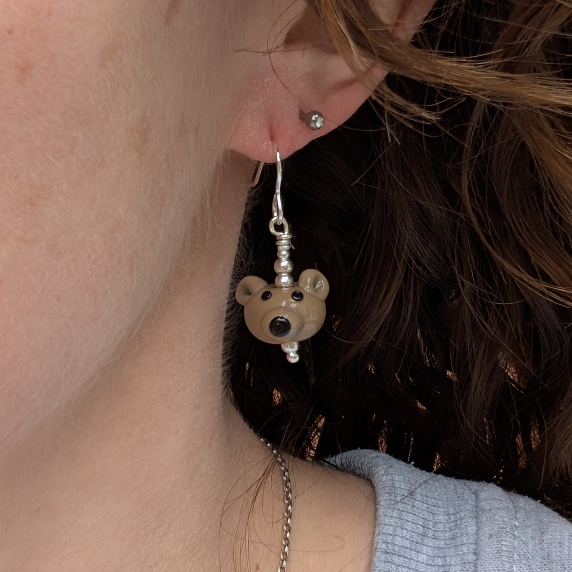 Side view of a person wearing one bear earring, showing its size and playful design.