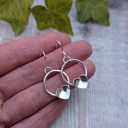 Circle earring with hammered hearts handmade from recycled Sterling Silver, shown resting on a hand to highlight the size and polished finish.