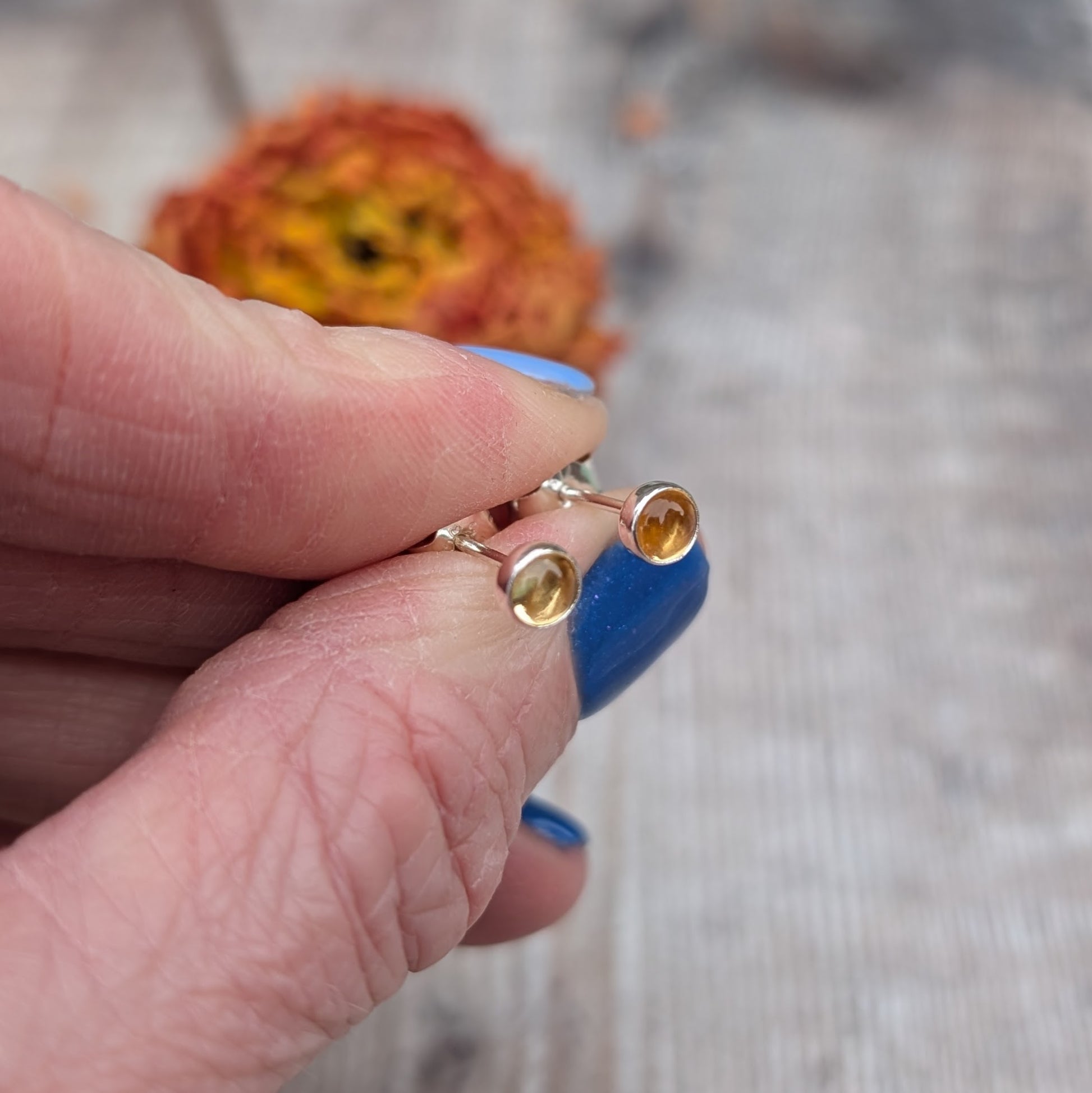 A pair of citrine stud earrings held in a hand, showing their compact design and shimmering gemstones.