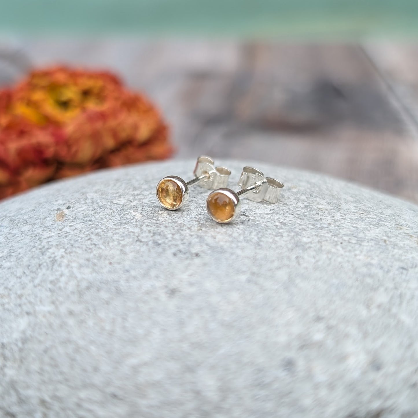 A close-up of citrine stud earrings resting on a smooth stone, showcasing their warm, golden glow against a soft background.