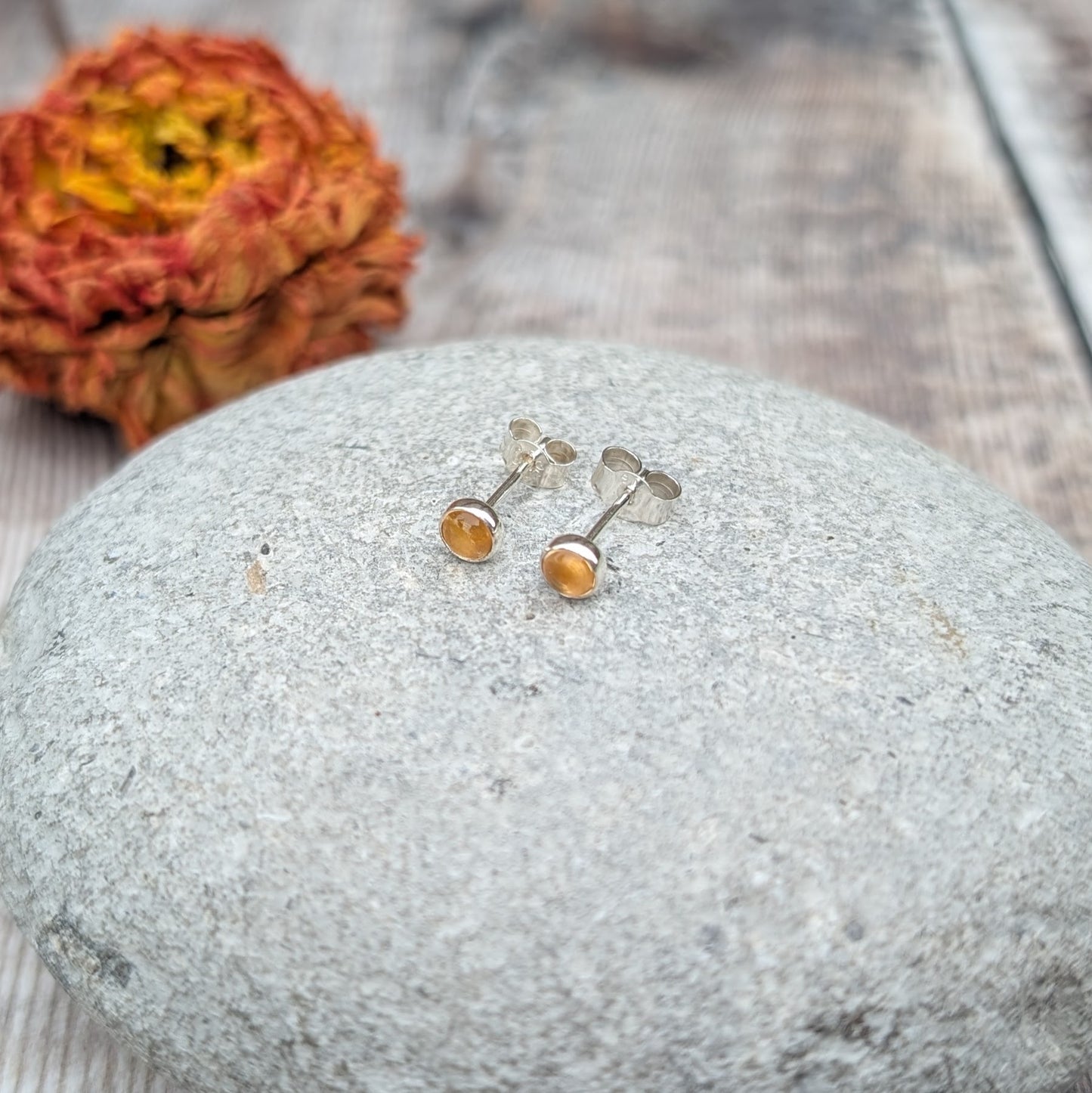 A close-up of citrine stud earrings resting on a smooth stone, showcasing their warm, golden glow against a soft background.