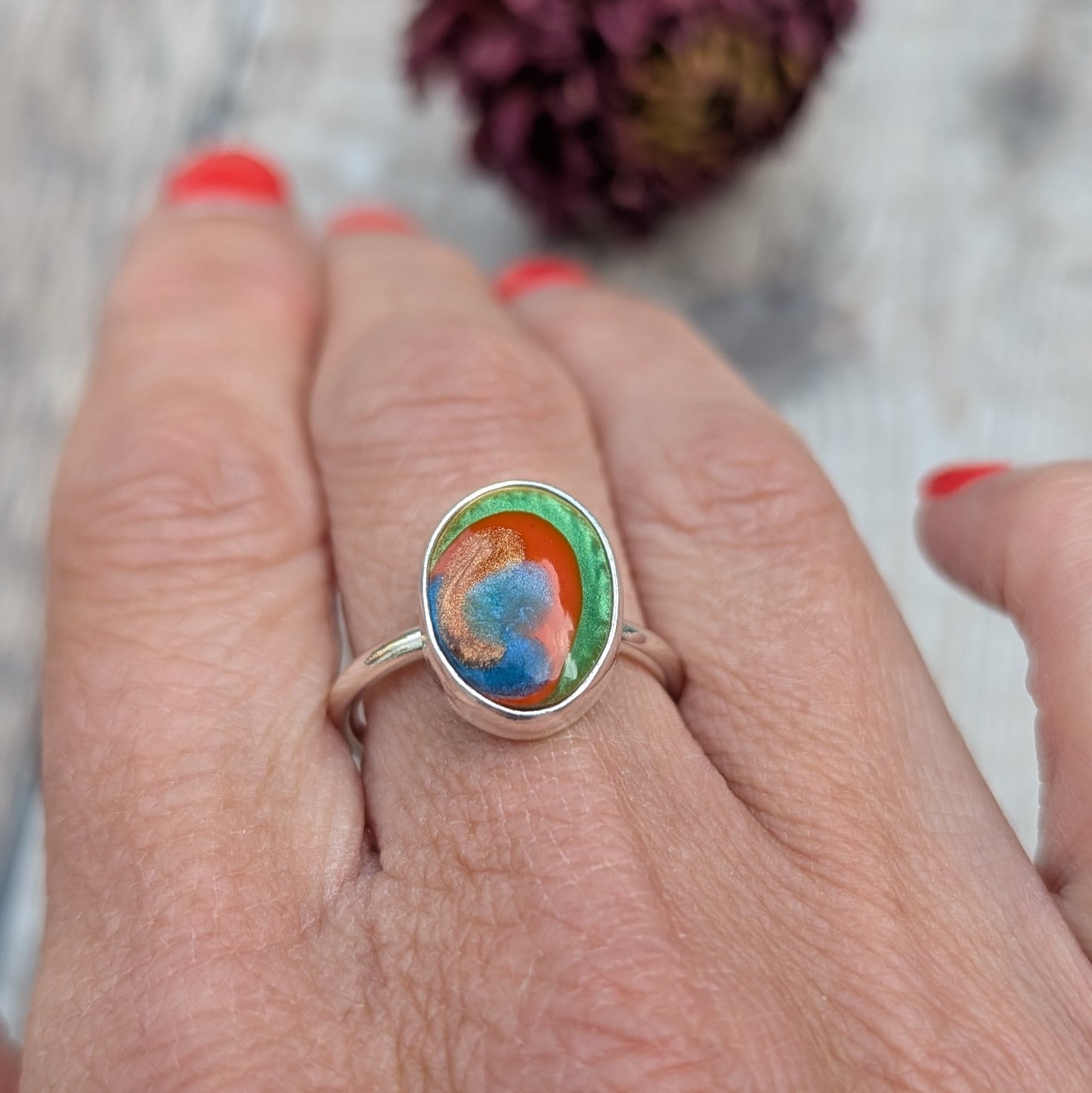 A colourful oval Surfite ring in recycled sterling silver, shown worn on a hand with red painted nails.