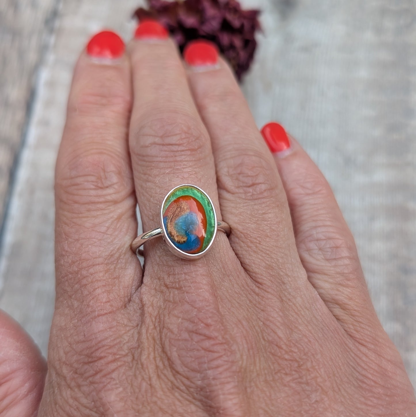 A colourful oval Surfite ring in recycled sterling silver, shown worn on a hand with red painted nails.
