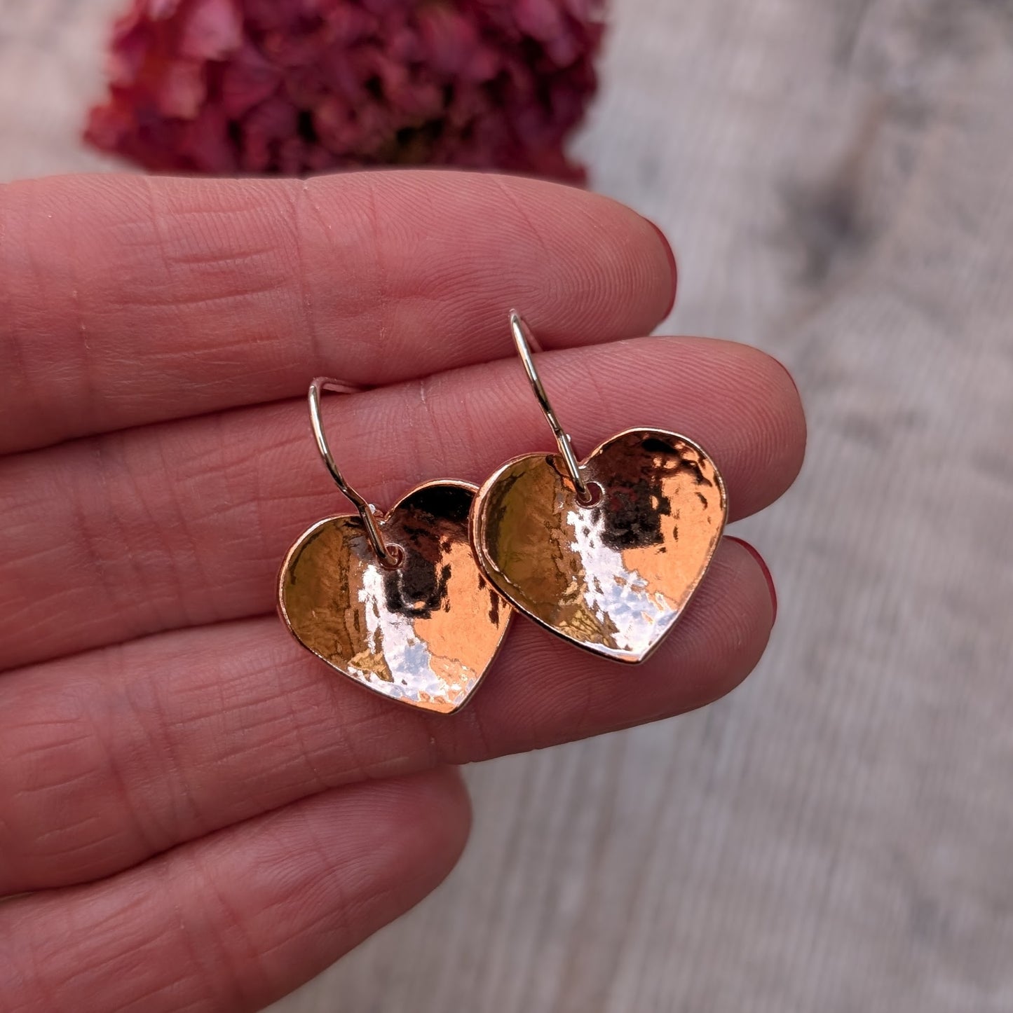 Two hammered copper heart earrings held together in a hand, highlighting their warm, polished finish.