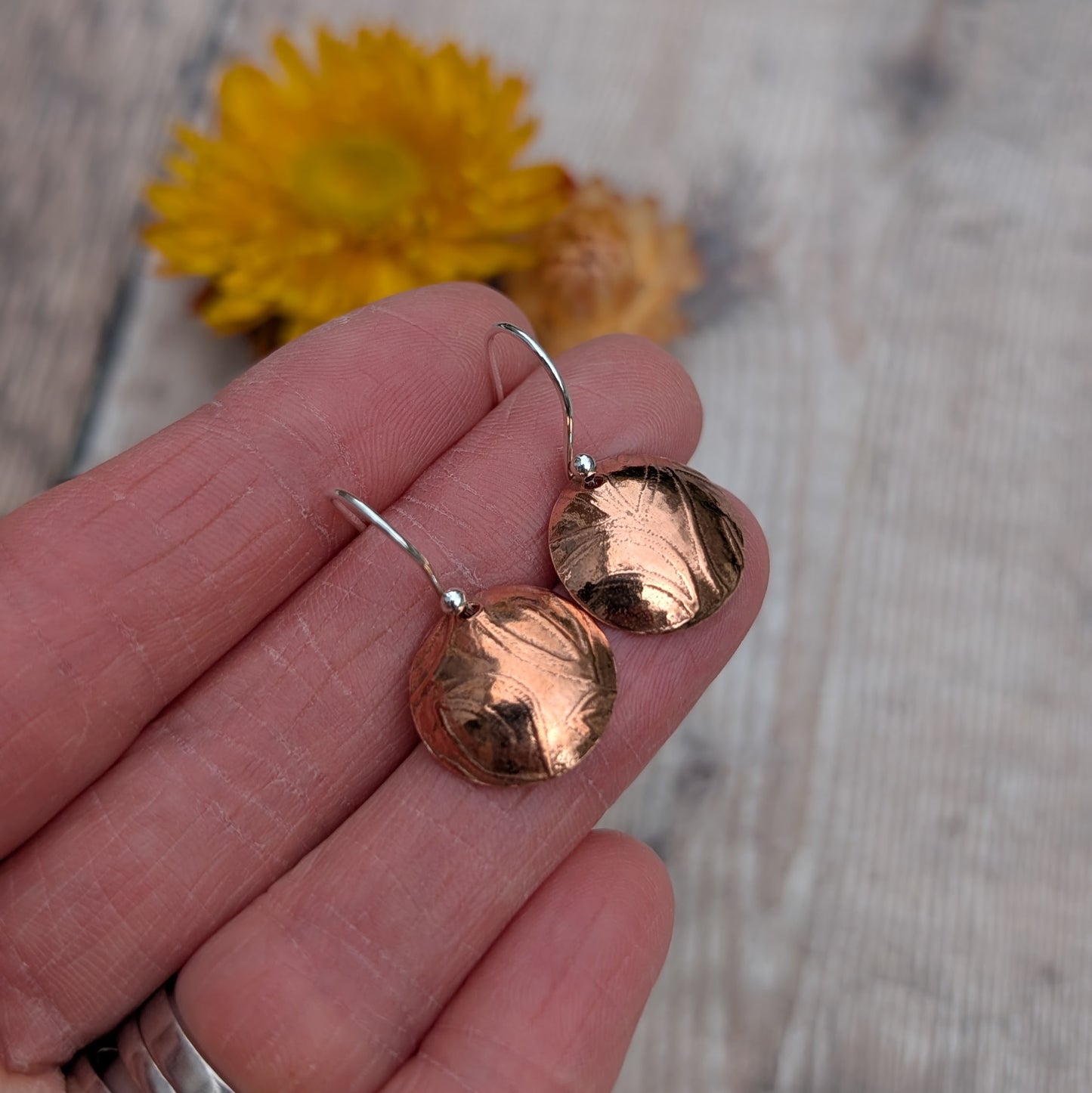 Copper large leaf pattern dome disc earrings shown close up in hand highlighting the pressed leaf pattern.