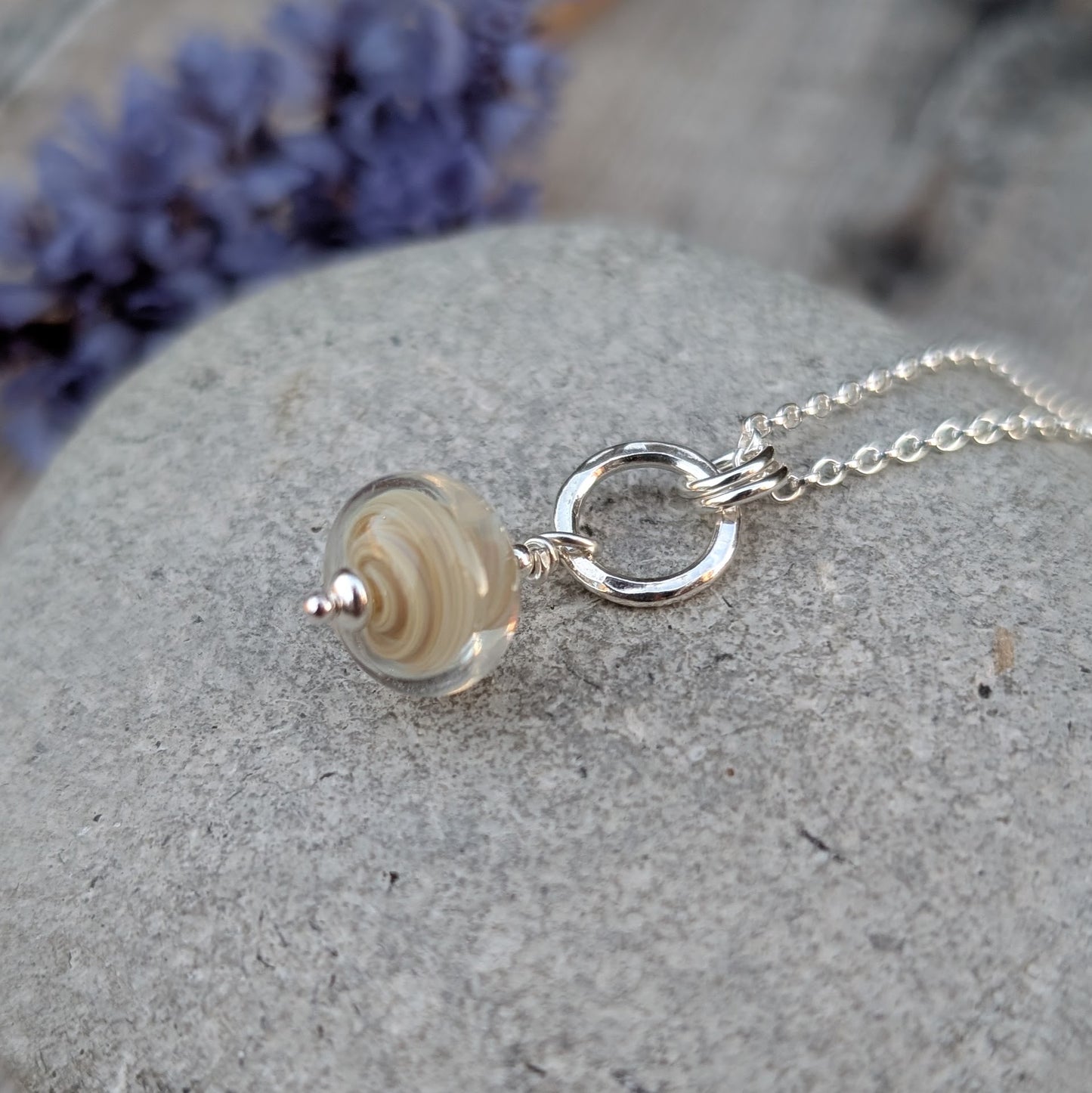 Close-up of the cream lampwork and silver circle necklace, focusing on the handmade glass bead and sterling silver fittings.