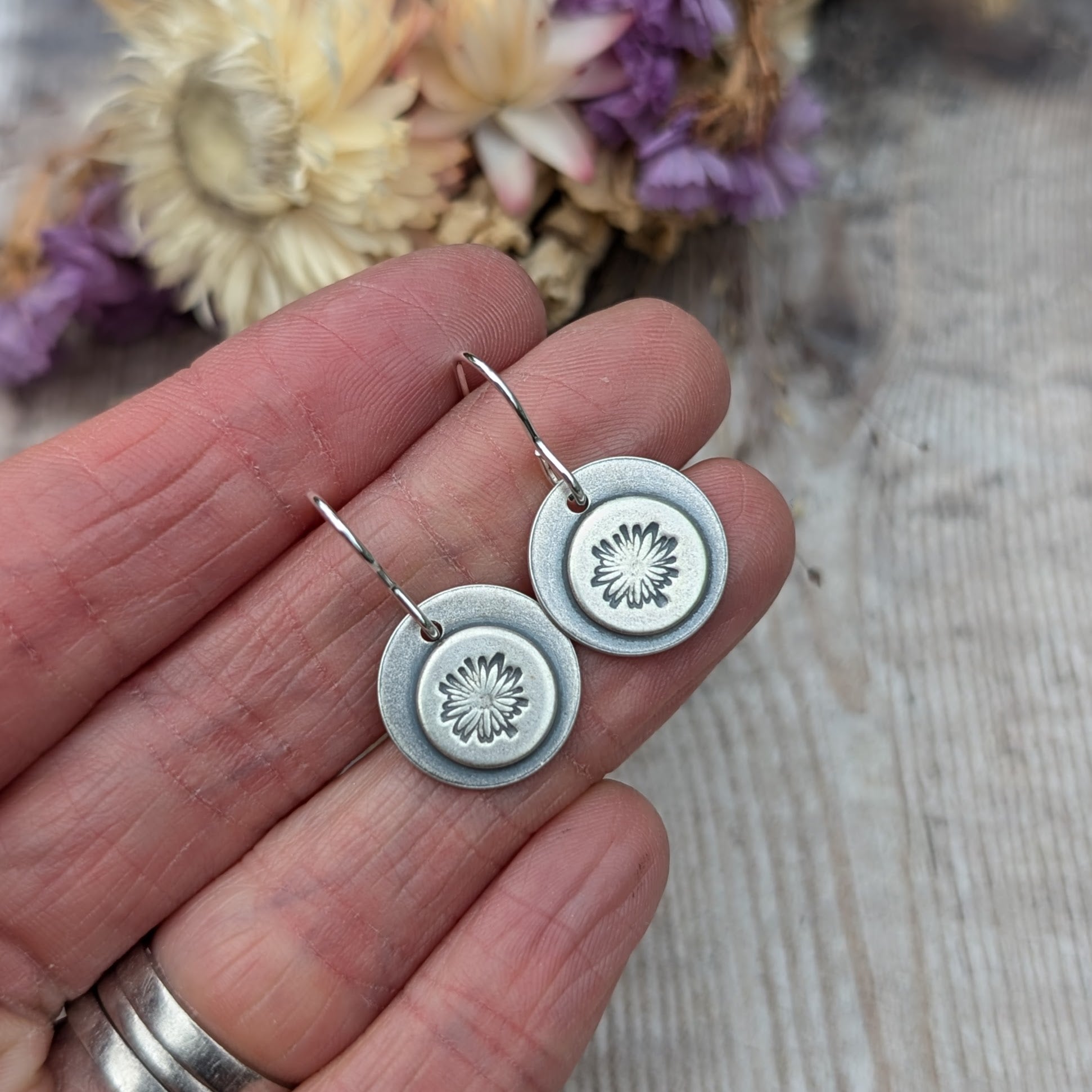 Handmade oxidised silver earrings with a daisy motif held in hand, showing the size and intricate detail of each disc.
