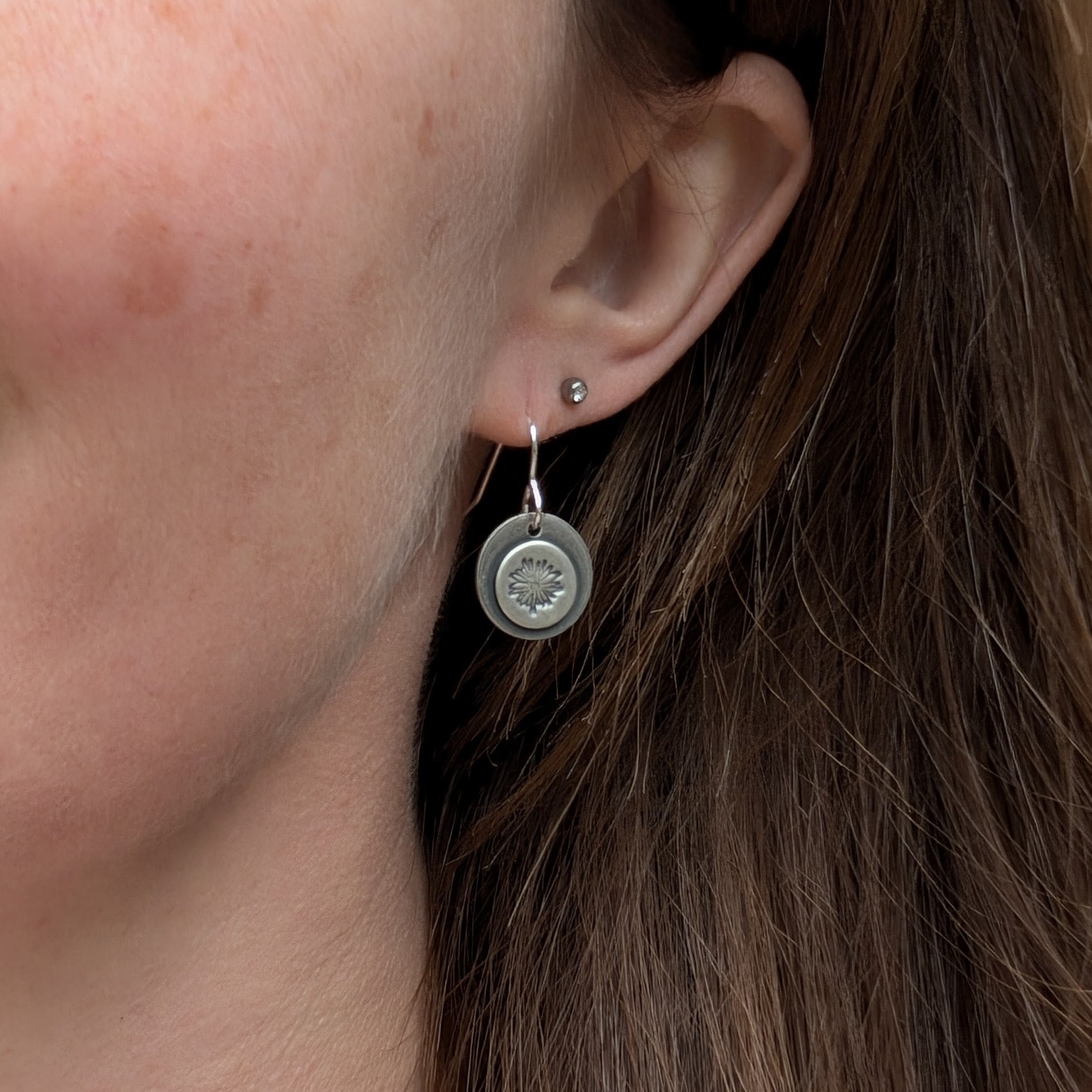 Oxidised silver daisy earrings worn on an ear, highlighting the lightweight and elegant design.