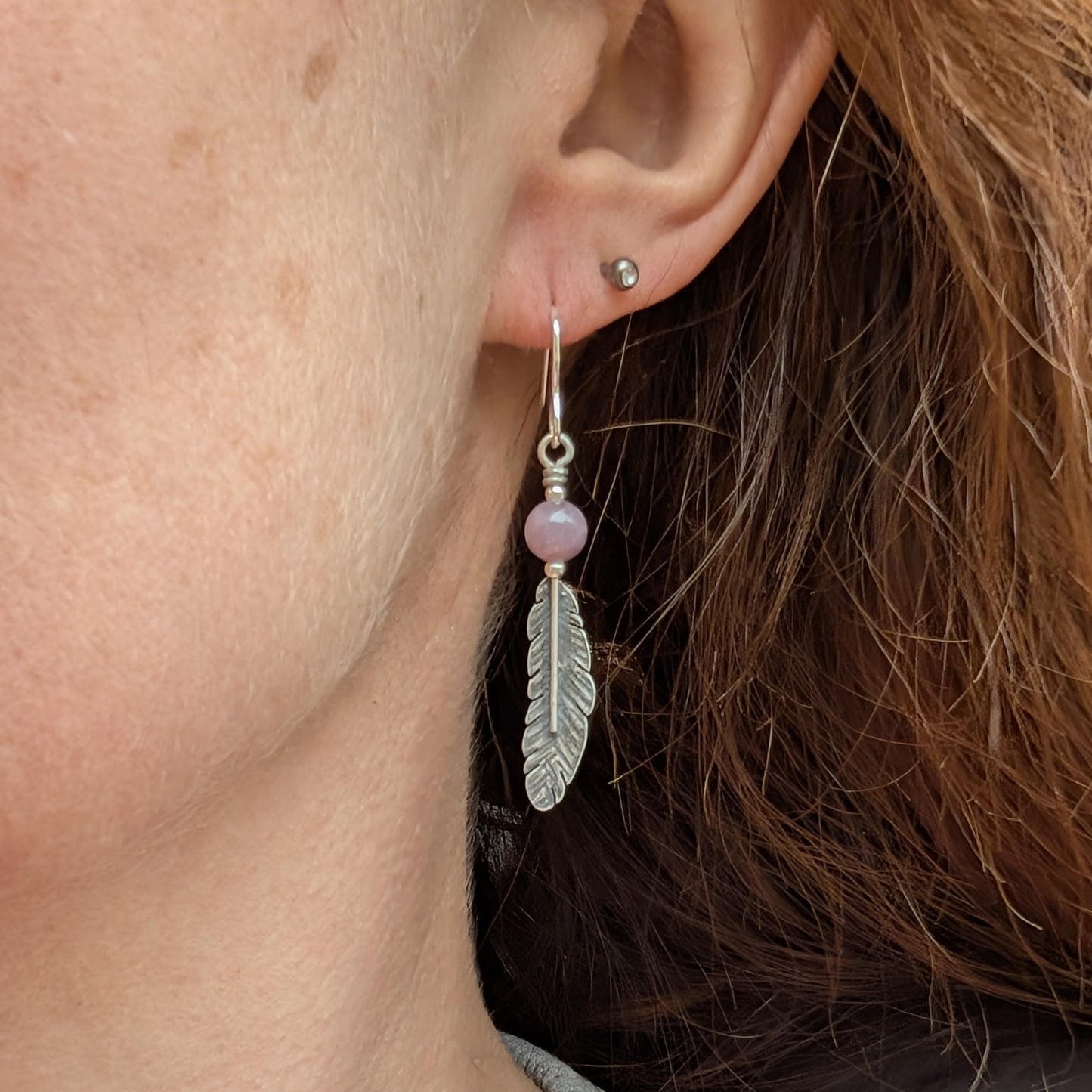 A side view of a woman wearing one of the silver feather earrings with a lavender amethyst bead, highlighting its length and delicate design.