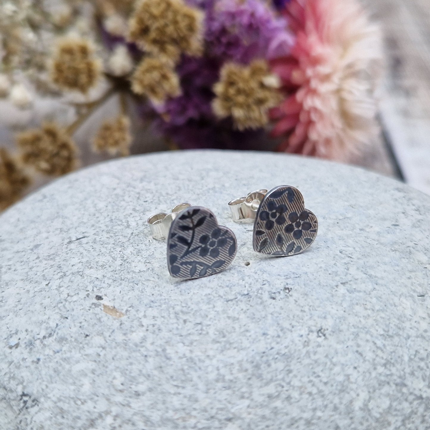 Each earring is an oxidised Sterling Silver heart shape on silver stud bar, stamped with a floral pattern of flowers with 5 petals and leaves.