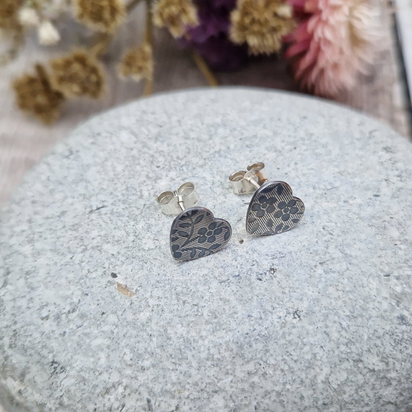 Each earring is an oxidised Sterling Silver heart shape on silver stud bar, stamped with a floral pattern of flowers with 5 petals and leaves.