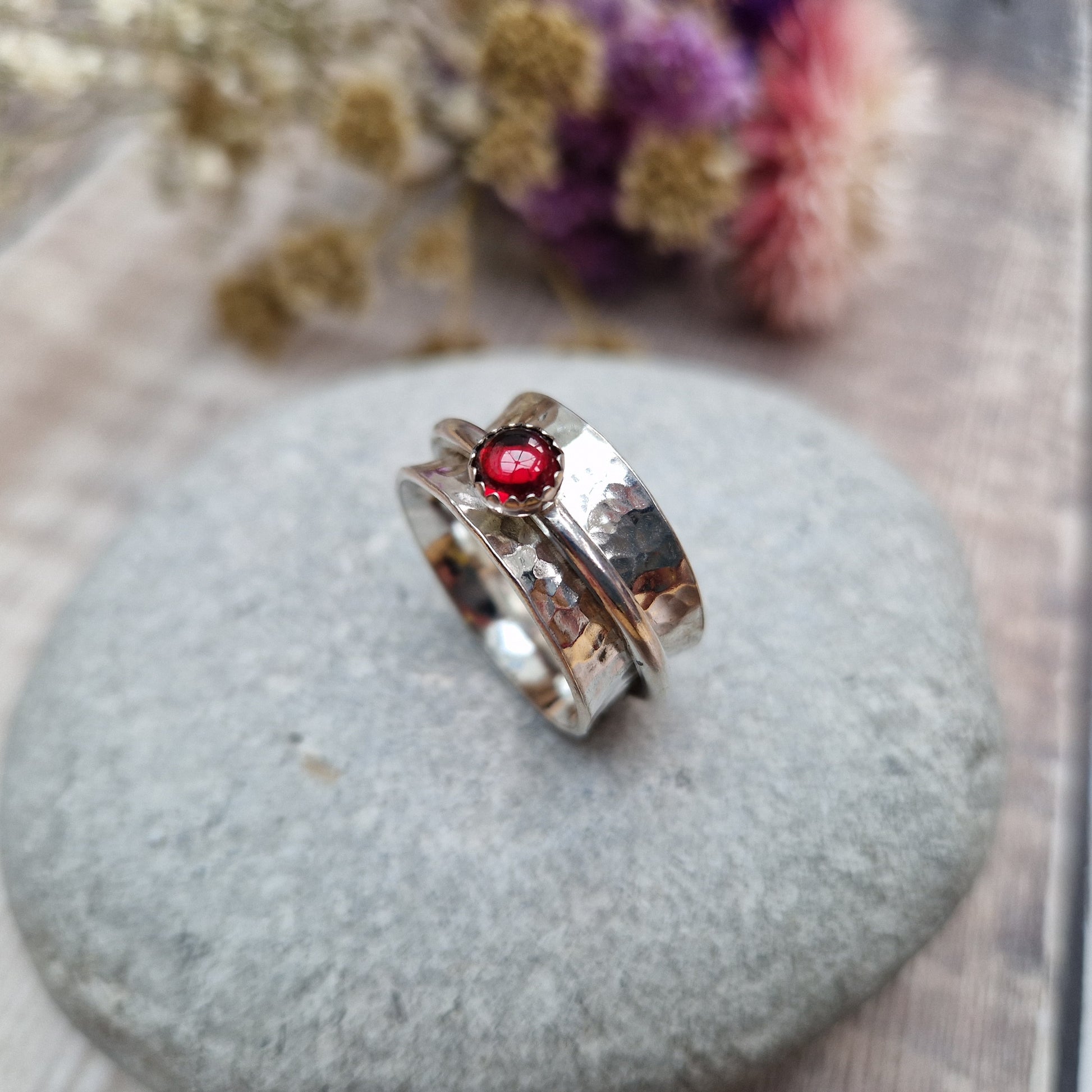 Approx. 10mm wide hammered texture silver band with additional 2mm wide silver band around the middle that spins independently. Mounted in a silver bezel on top of the 2mm wide band is a round red garnet gemstone, approx. 5mm diameter.