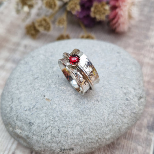 Approx. 10mm wide hammered texture silver band with additional 2mm wide silver band around the middle that spins independently. Mounted in a silver bezel on top of the 2mm wide band is a round red garnet gemstone, approx. 5mm diameter.