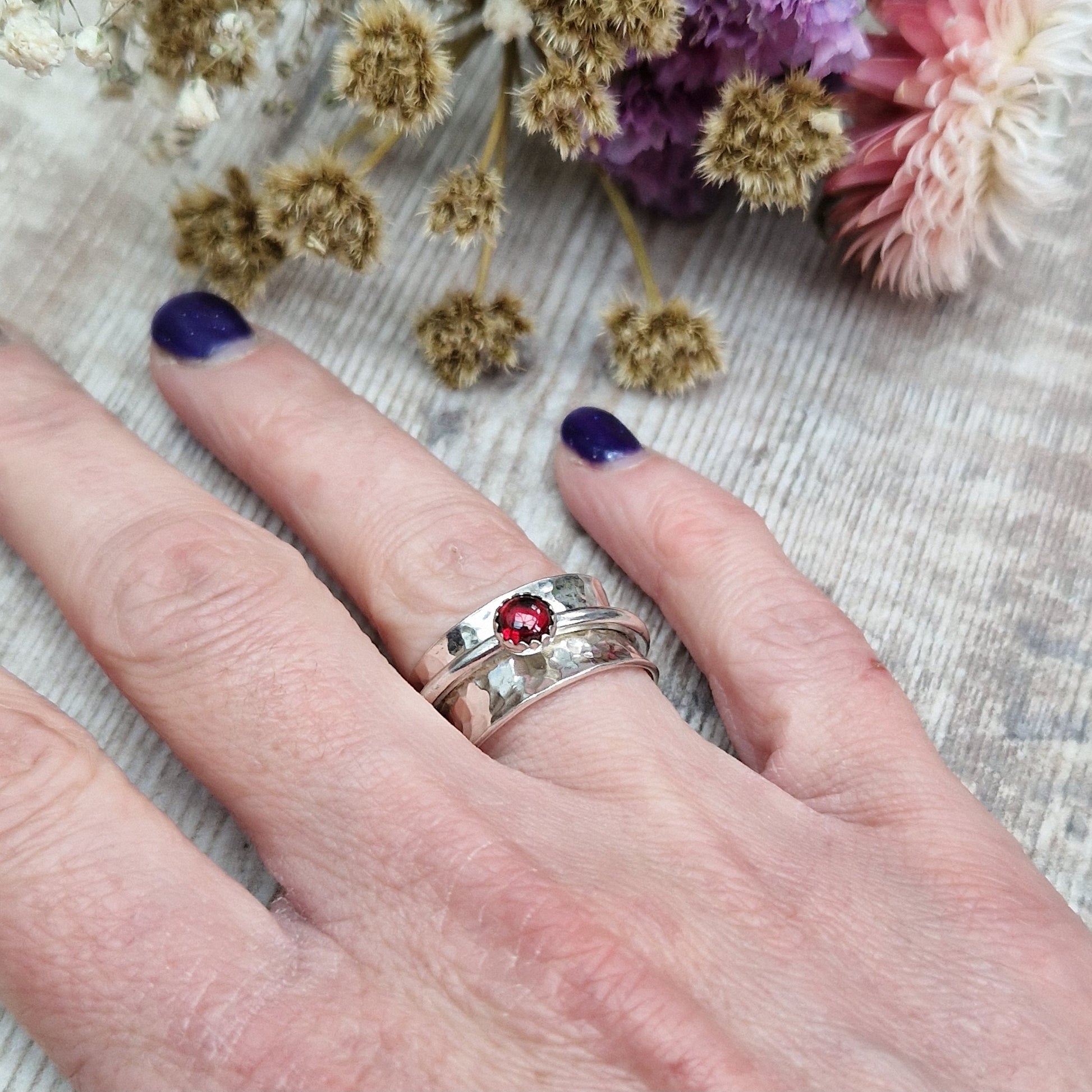 Approx. 10mm wide hammered texture silver band with additional 2mm wide silver band around the middle that spins independently. Mounted in a silver bezel on top of the 2mm wide band is a round red garnet gemstone, approx. 5mm diameter.