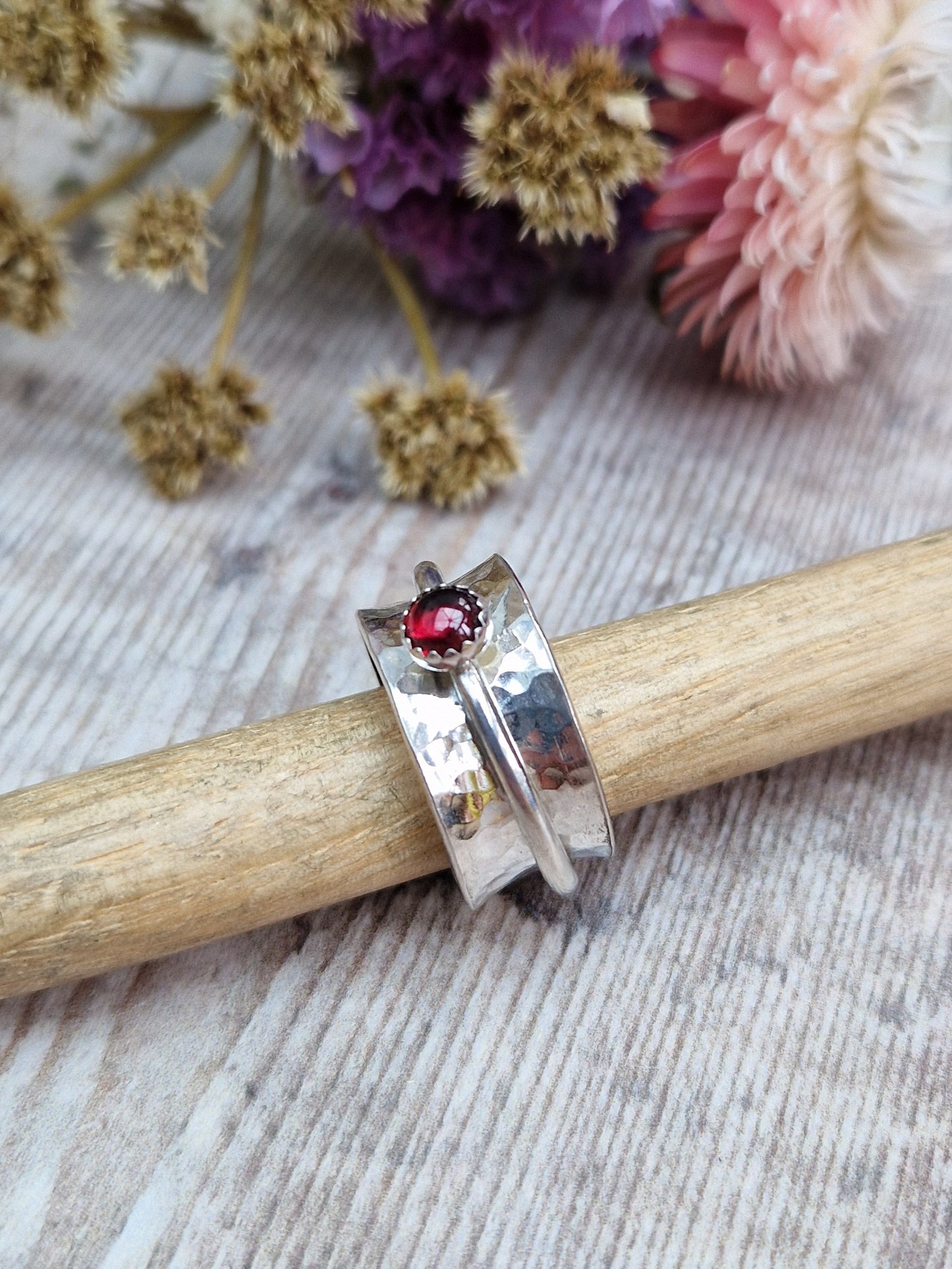 Approx. 10mm wide hammered texture silver band with additional 2mm wide silver band around the middle that spins independently. Mounted in a silver bezel on top of the 2mm wide band is a round red garnet gemstone, approx. 5mm diameter.
