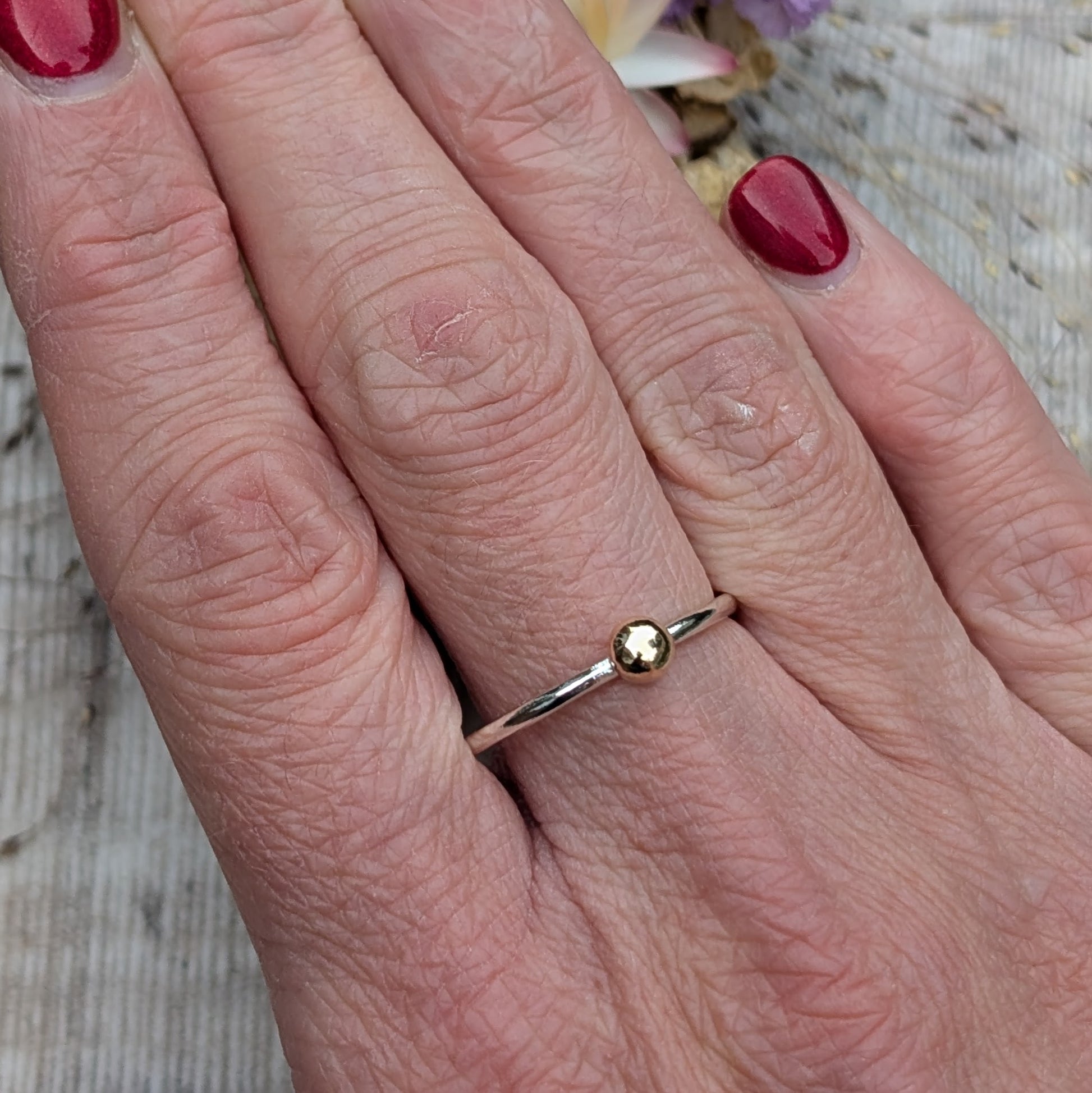 A simple silver and gold pebble ring worn on a finger, showcasing its dainty and understated style, perfect for stacking or wearing alone.