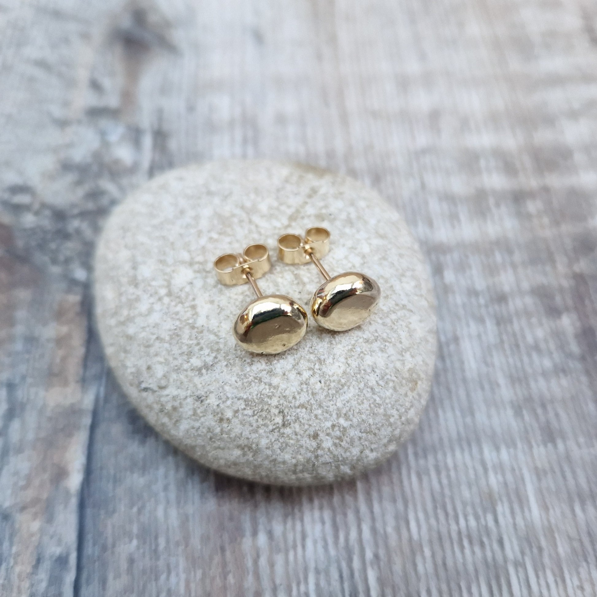 9ct gold pebble shape stud earrings. Recycled 9ct gold melted into a smooth, imperfect round pebble shape with small imperfections on the surface of the gold to provide subtle interest. Each pebble shape measuring approximately 8mm x 7mm, mounted on gold earring bar.