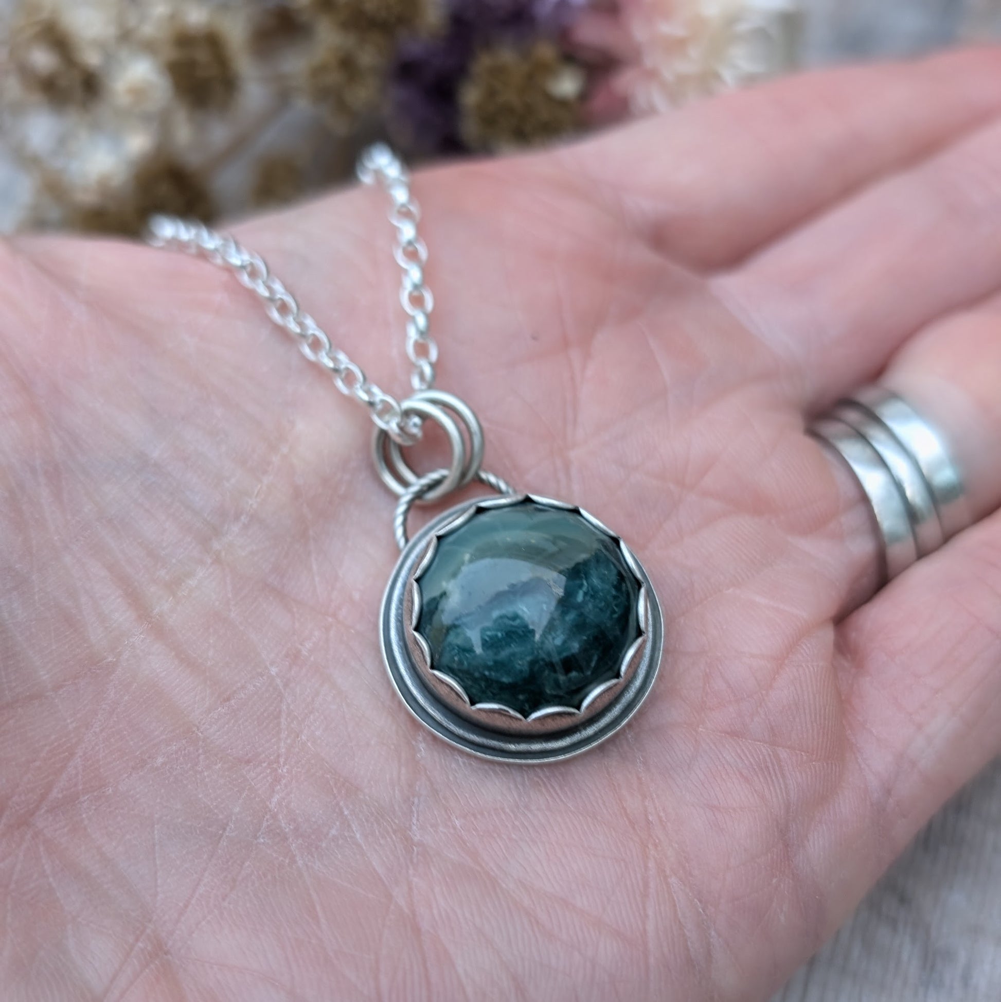 A Green Hava Ridge Jasper necklace held in an open hand, highlighting the size and intricate detailing of the recycled silver setting.