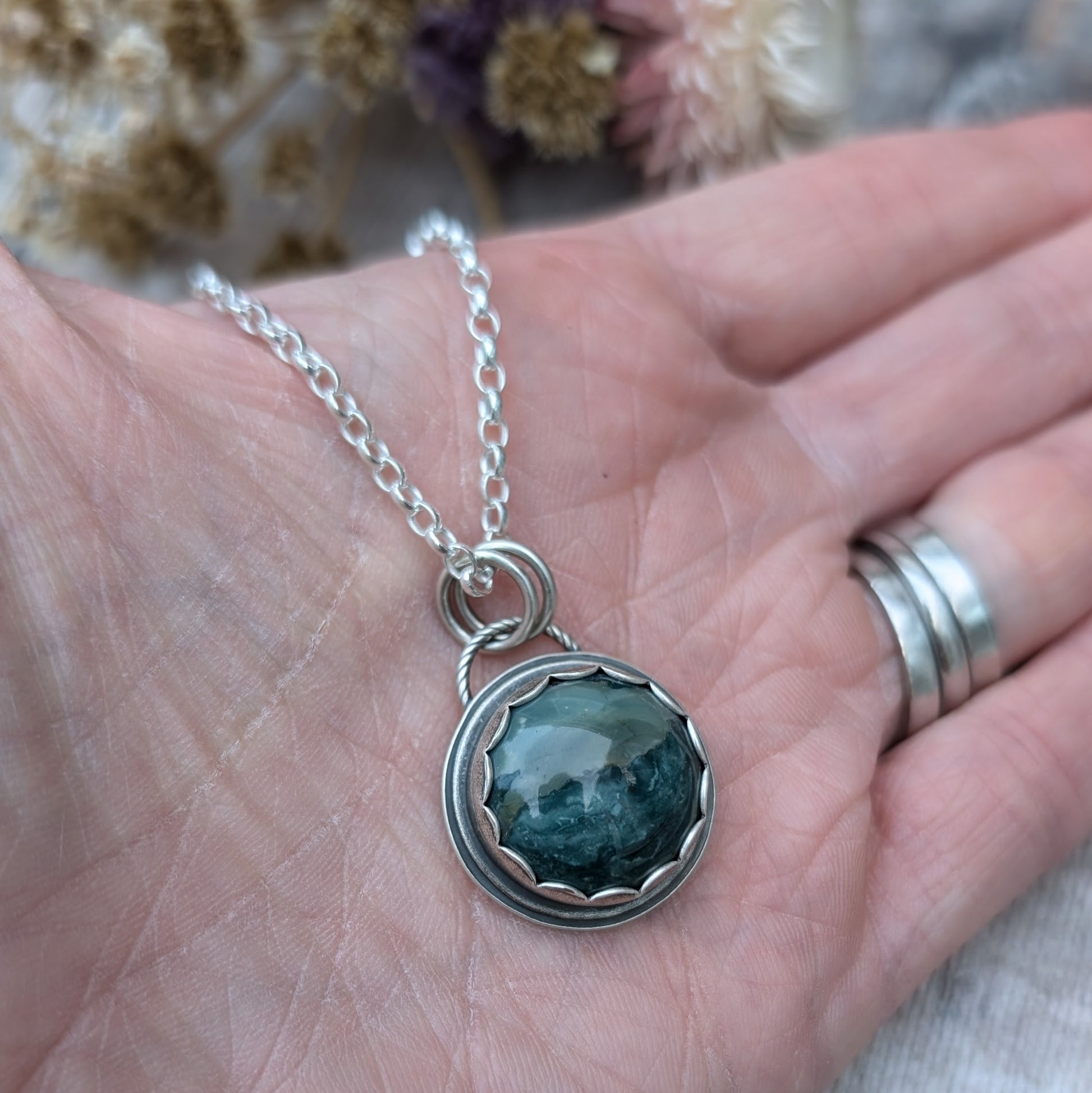 A Green Hava Ridge Jasper necklace held in an open hand, highlighting the size and intricate detailing of the recycled silver setting.