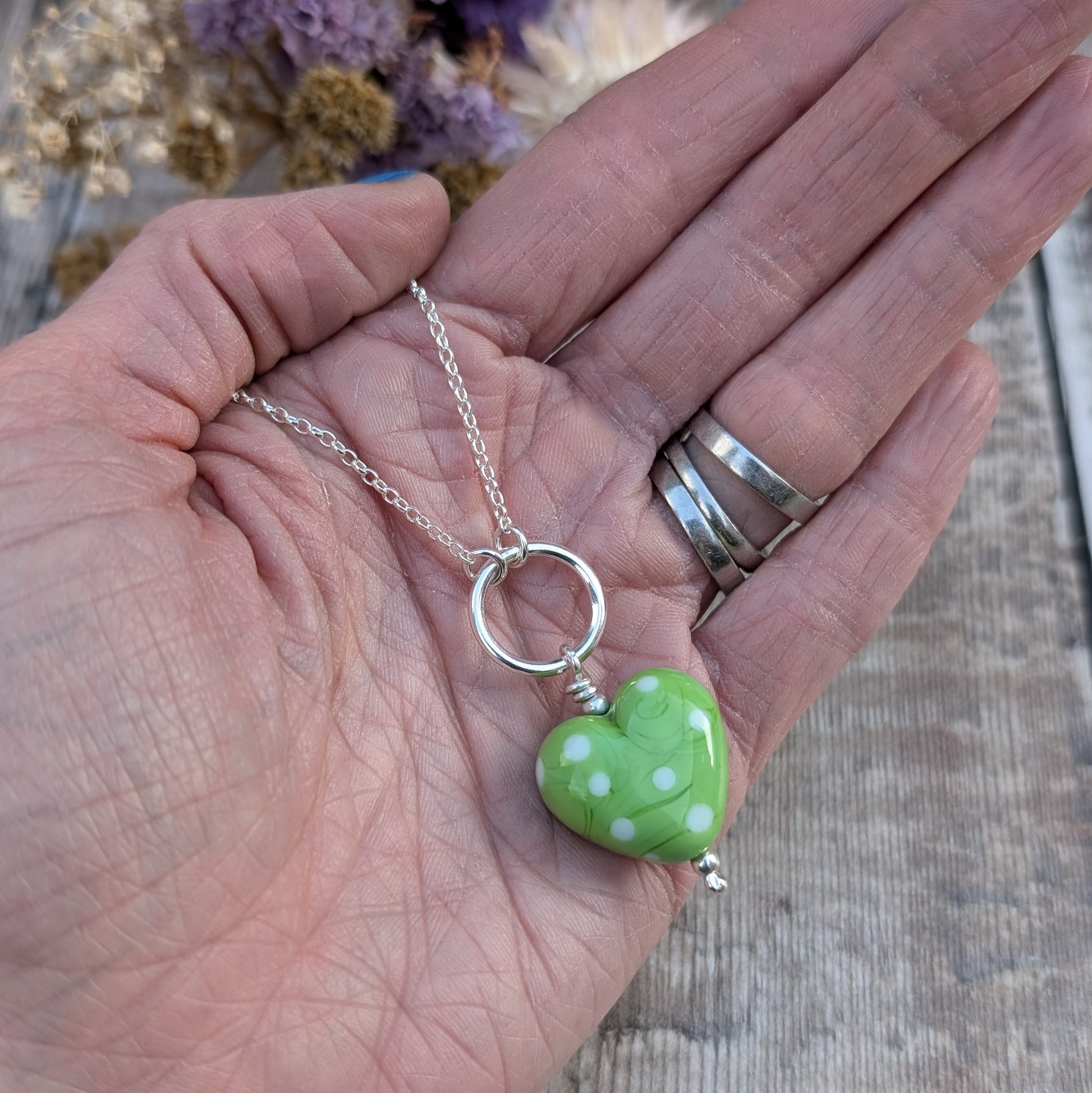 A green polka-dot Lampwork glass heart necklace with a sterling silver circle, shown in the palm of a hand to illustrate its size and detail.