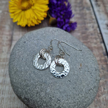 Load image into Gallery viewer, Sterling Silver hammered circle drop earrings. Attached to silver earring wire via two small silver hoops is a silver disc with hole cut out of the middle, making a thick circle shape with hammered texture. Disc measuring approximately 15mm diameter. Total drop from earlobe approximately 35mm providing lots of movement.