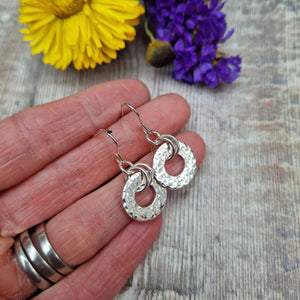 Sterling Silver hammered circle drop earrings. Attached to silver earring wire via two small silver hoops is a silver disc with hole cut out of the middle, making a thick circle shape with hammered texture. Disc measuring approximately 15mm diameter. Total drop from earlobe approximately 35mm providing lots of movement.