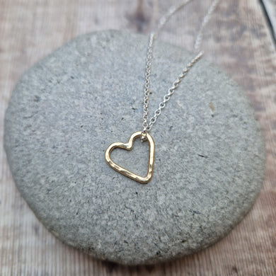 Open heart shaped 9ct gold pendant hangs from sterling silver chain necklace. Heart measures approximately 15mm diameter. Slightly hammered texture on the pendant.