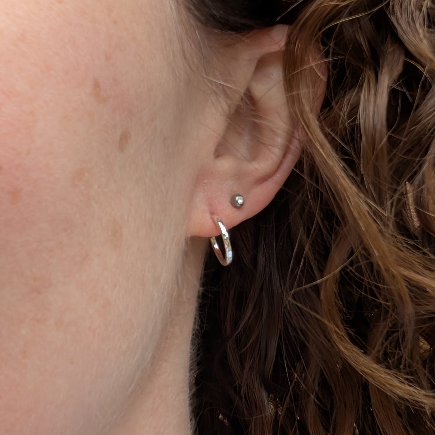 Close-up of small hammered silver hoop earring worn in a lobe piercing.