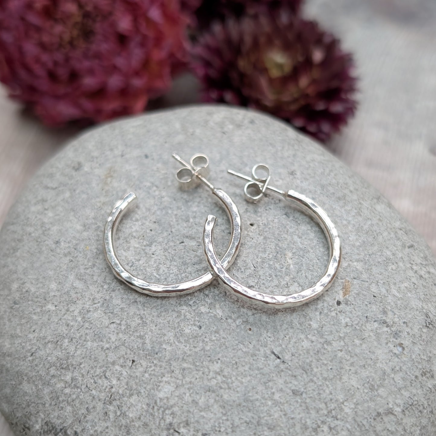Pair of hammered sterling silver hoop earrings displayed on a stone, highlighting their round shape and handcrafted finish.