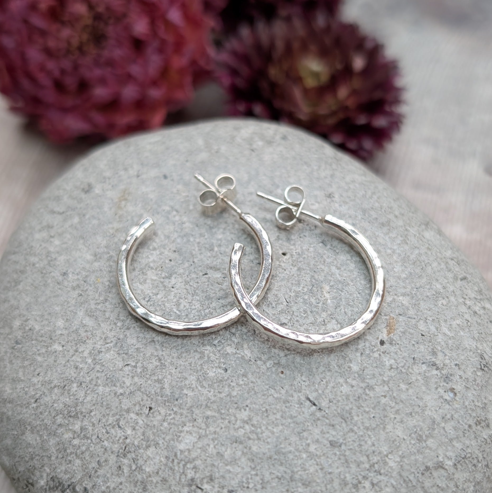 Pair of hammered sterling silver hoop earrings displayed on a stone, highlighting their round shape and handcrafted finish.