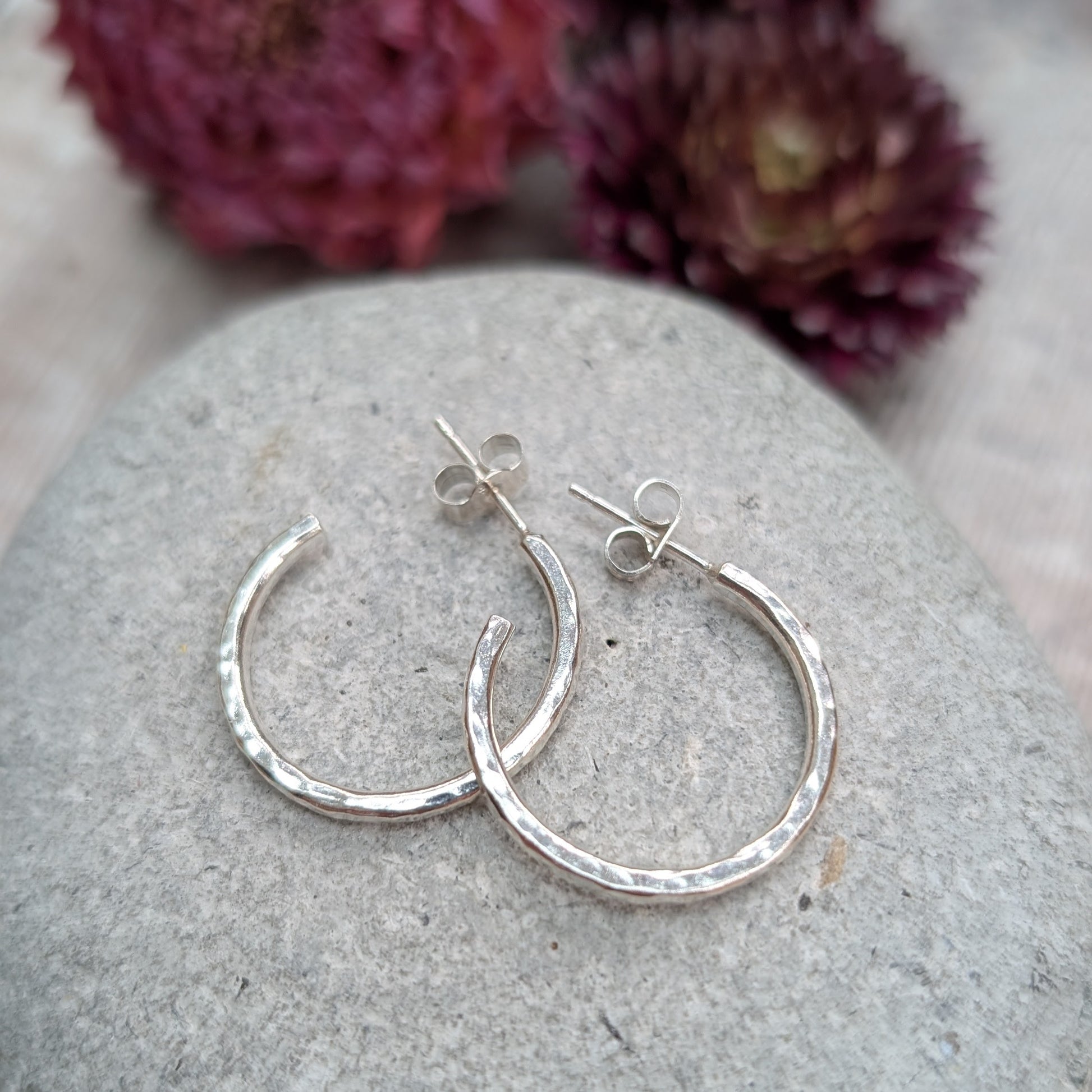 Pair of hammered sterling silver hoop earrings displayed on a stone, highlighting their round shape and handcrafted finish.