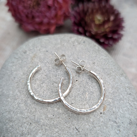 Pair of hammered sterling silver hoop earrings displayed on a stone, highlighting their round shape and handcrafted finish.