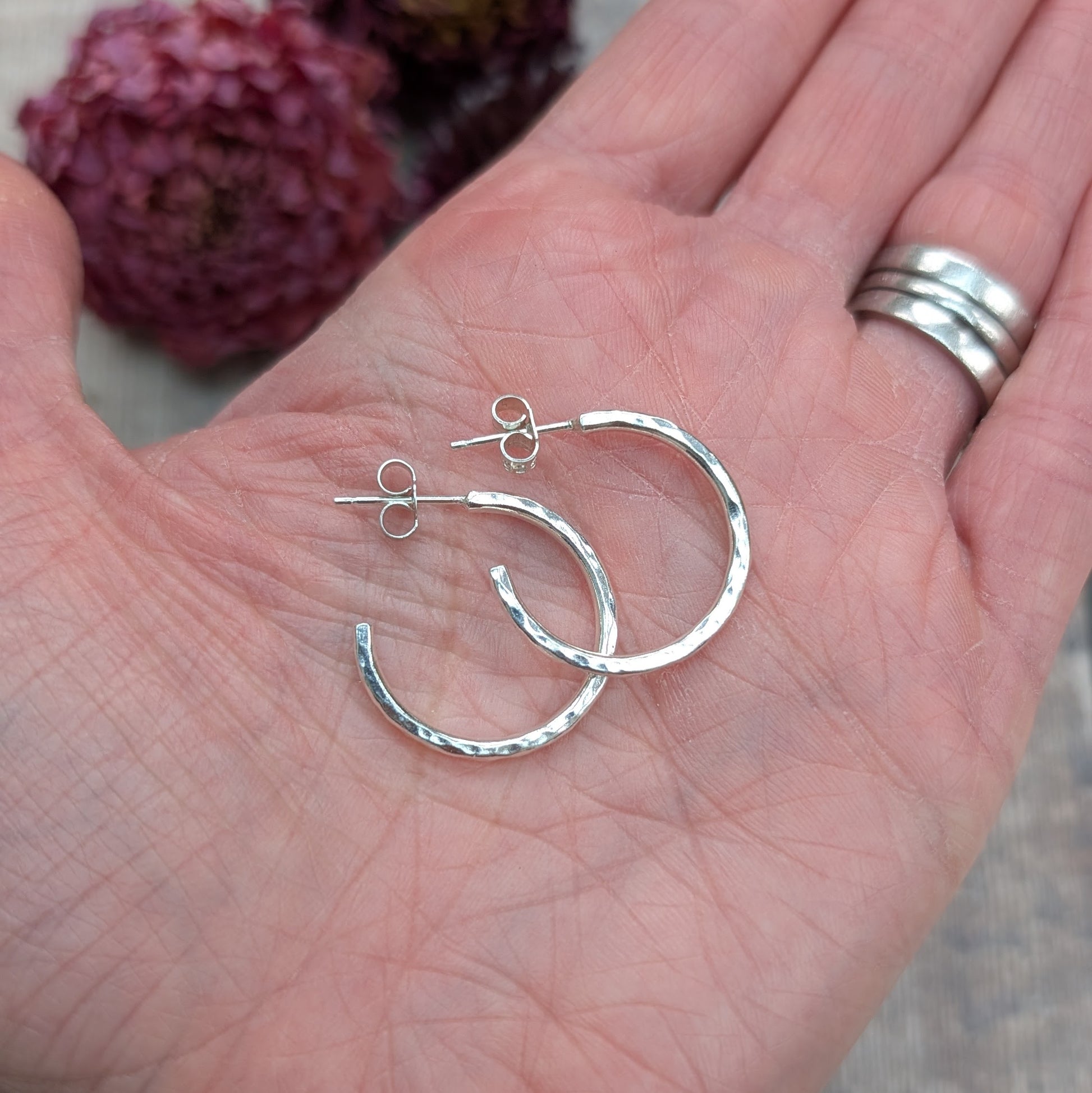 Hand holding a pair of 20mm hammered recycled sterling silver hoop earrings, showing scale and texture.