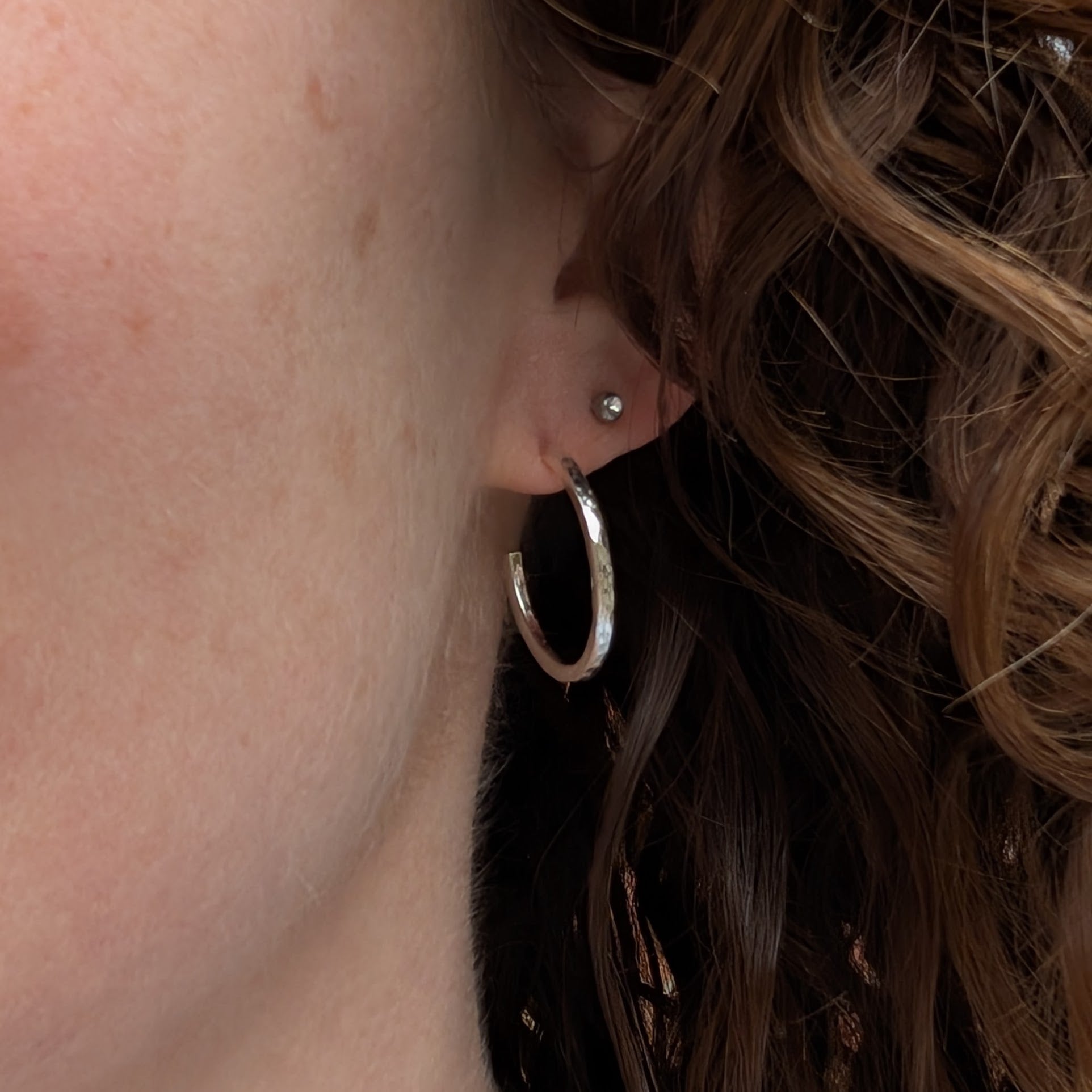 Close-up of a single hammered silver hoop earring worn in the ear, showing its medium size and shine.
